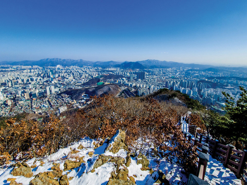 관모봉에서 바라본 안양시와 군포시 전경. 도심 너머 가운데 모락산이 솟아 있고, 그 너머로 청계산, 바라산, 광교산이 장대한 산줄기를 잇는다.