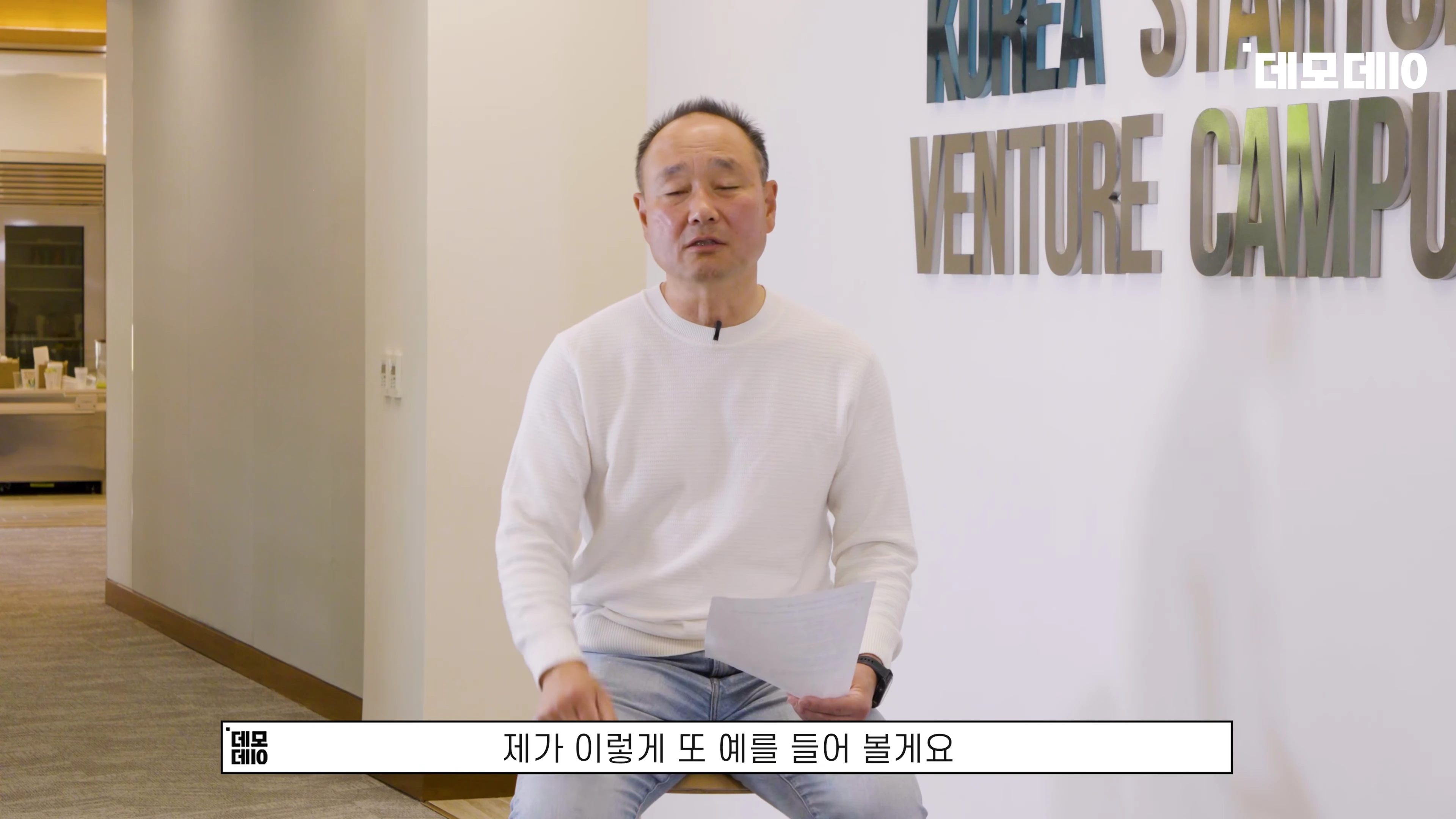 흰색 니트를 입은 남성이 사무실 복도에서 대담을 나누는 모습