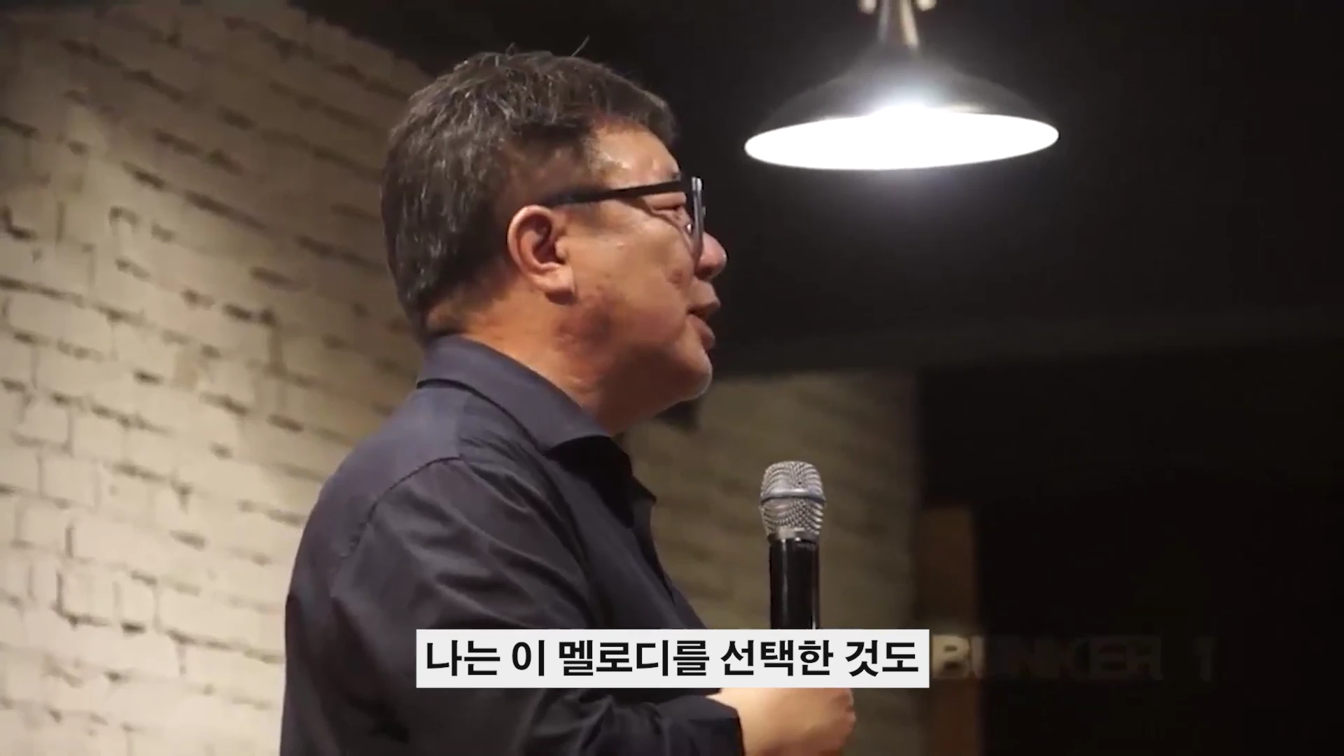 마이크를 잡고 강연하는 남성의 옆모습을 담은 강연 장면