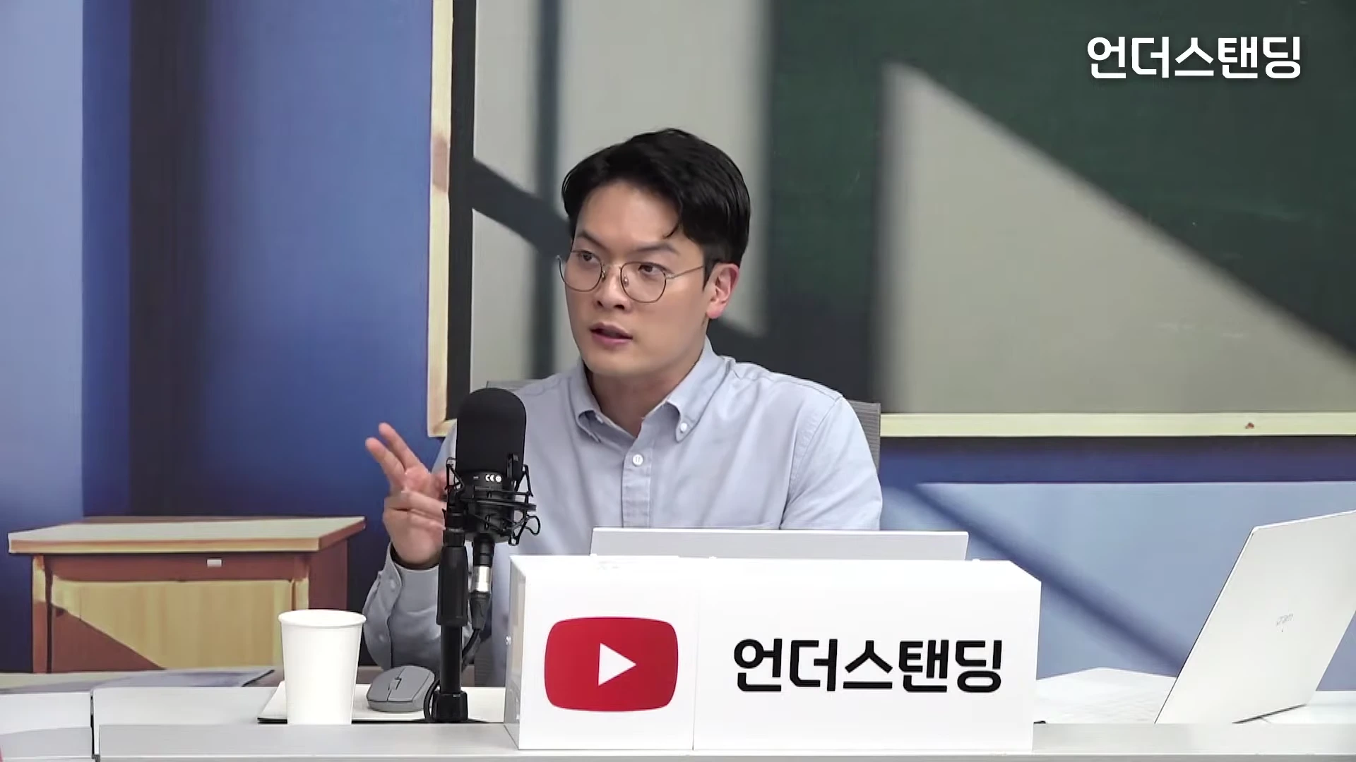 안경을 쓴 남성이 마이크 앞에서 손짓하며 대화하는 인터뷰 장면