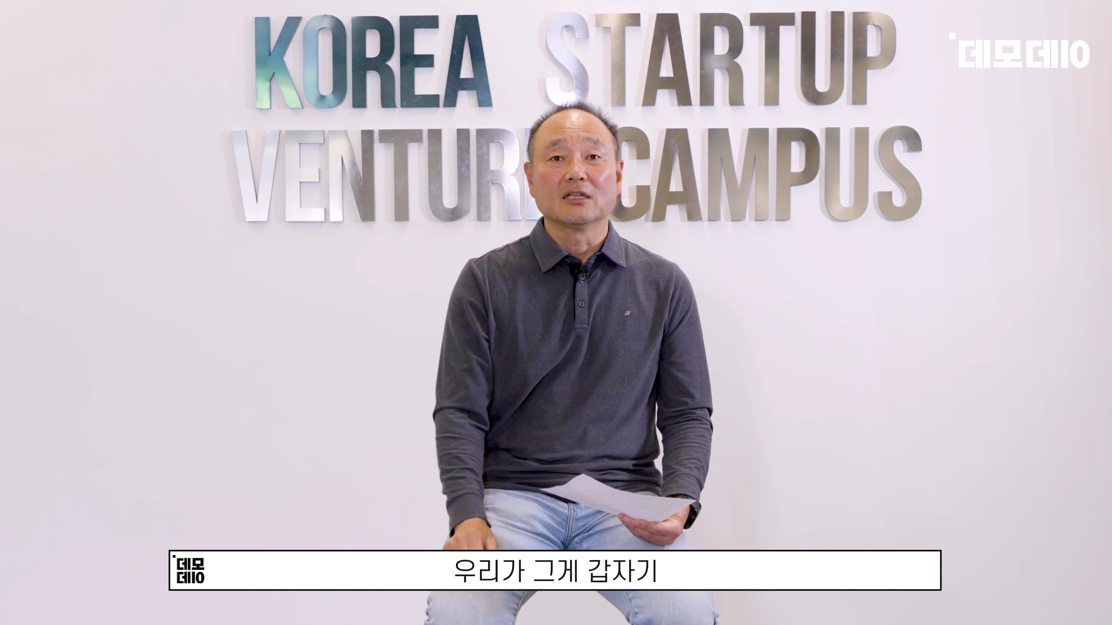 흰 벽에 'KOREA STARTUP VENTURE CAMPUS'라는 글자가 붙어 있고, 그 앞에 중년 남성이 앉아 이야기하고