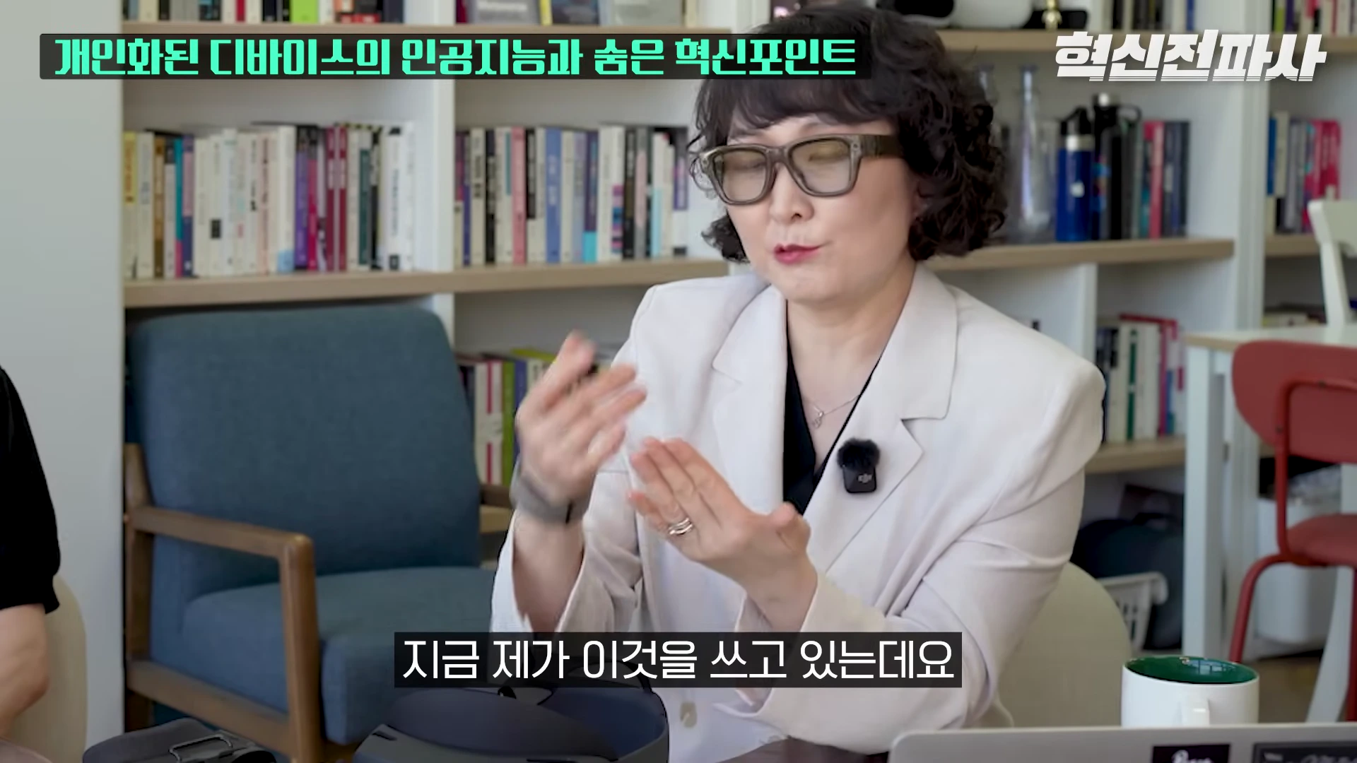 안경을 쓴 여성이 서재를 배경으로 손동작을 하며 대화하고 있는 모습