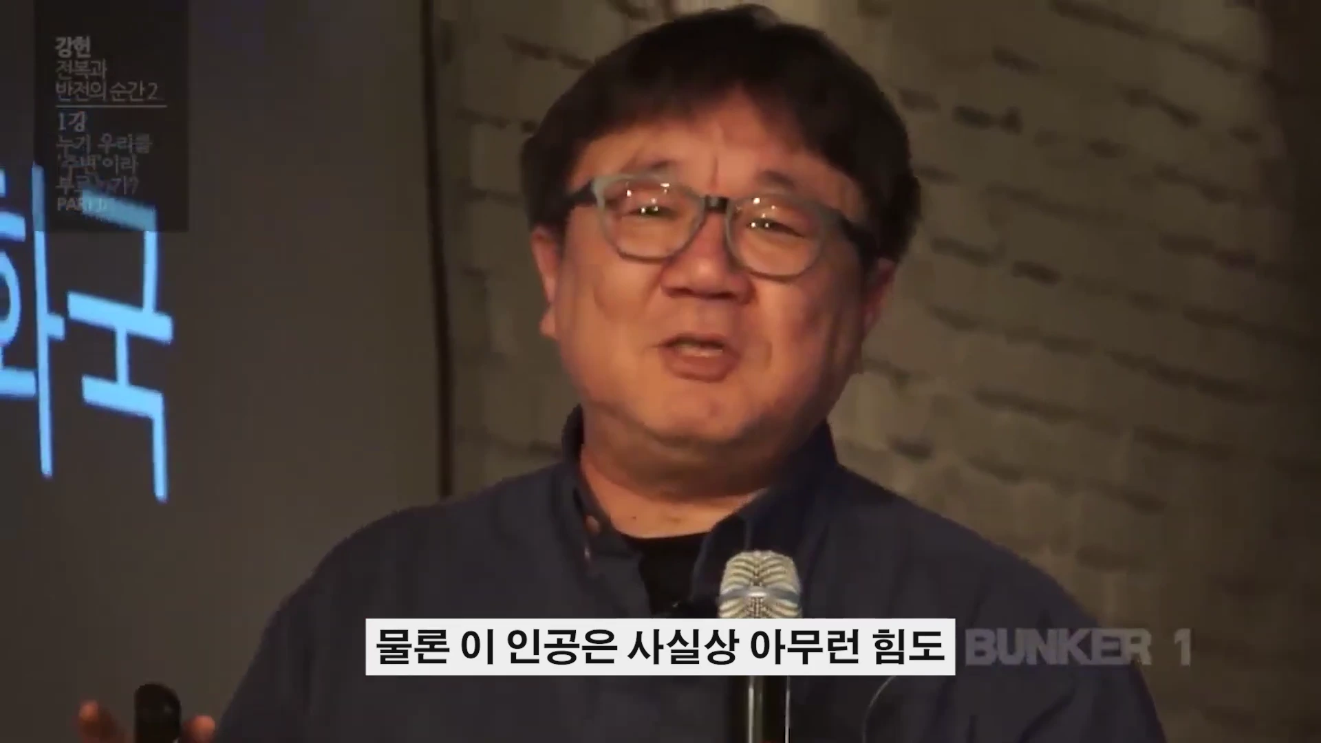 안경을 쓴 중년 남성이 마이크를 잡고 강연하는 모습