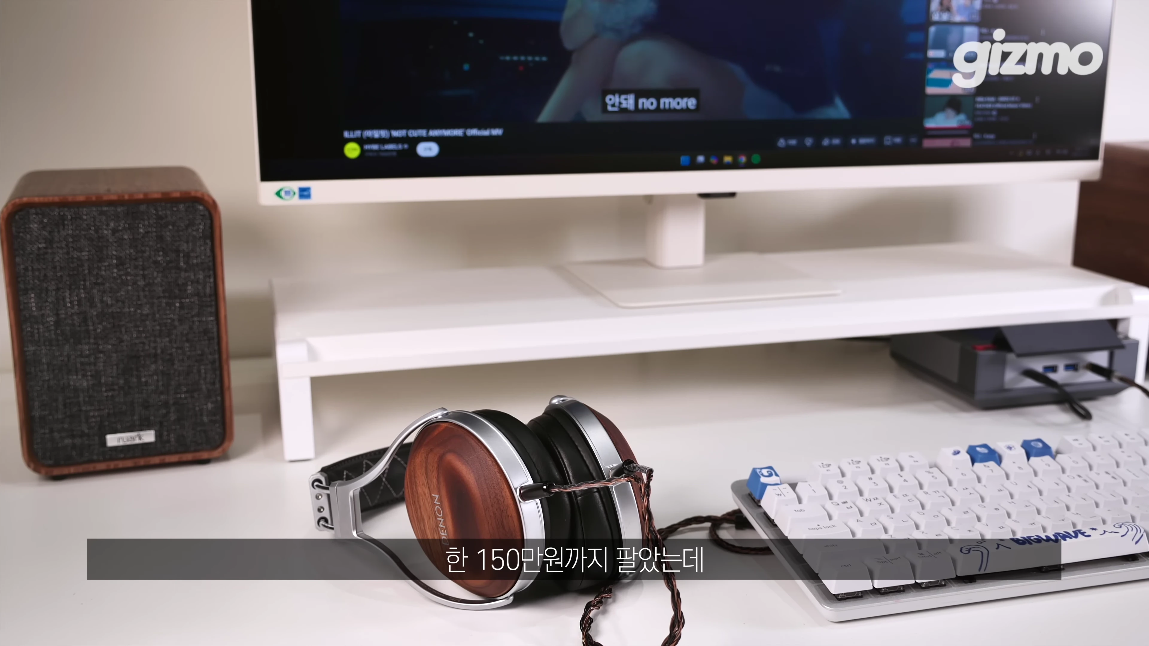 책상 위에 놓인 원목 디자인의 헤드폰과 스피커, 그리고 흰색 키보드와 모니터가 보이는 데스크테리어 환경.