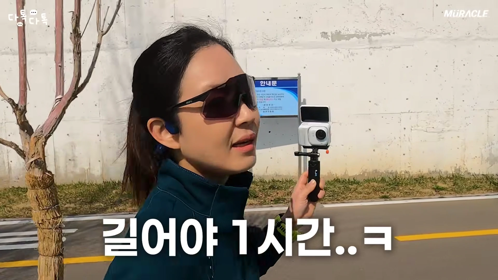 선글라스를 쓴 여성이 야외에서 액션캠을 들고 촬영하며 이야기하는 모습