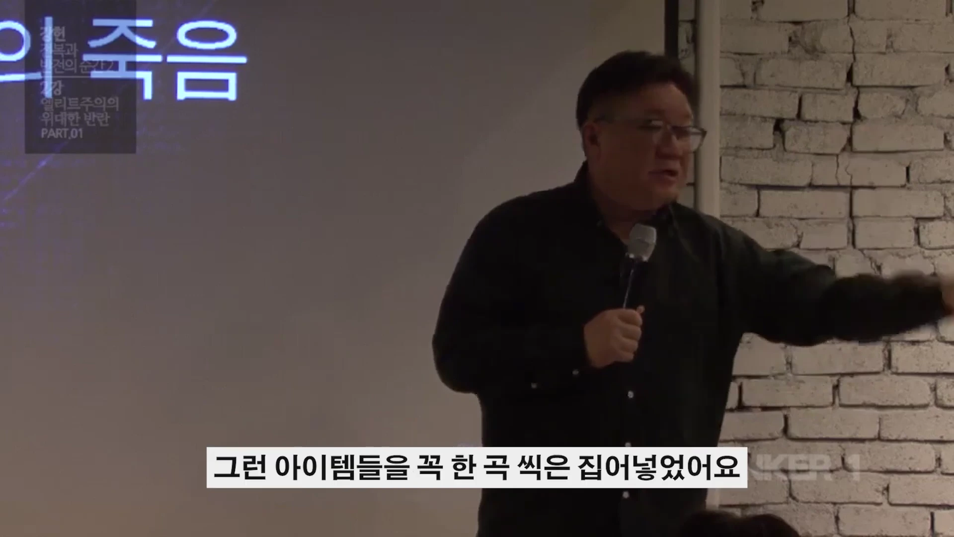 안경을 쓴 남성이 마이크를 들고 강연하는 모습