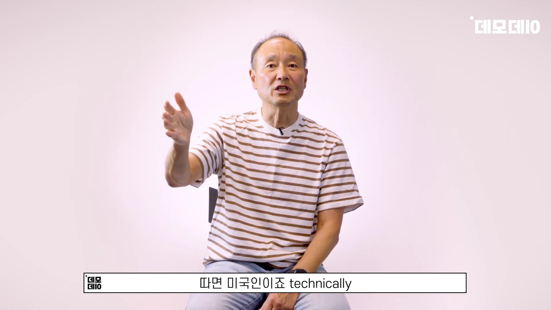 흰색 배경 앞에서 줄무늬 티셔츠를 입은 중년 남성이 손을 들어 제스처를 하며 이야기하고 있다.