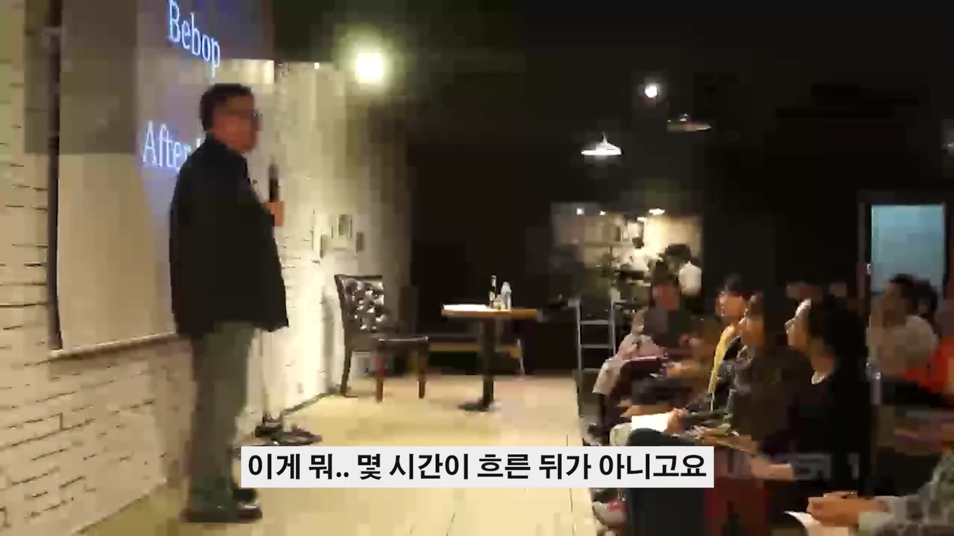 강연자가 스크린 앞에 서서 청중을 향해 마이크를 잡고 이야기하는 강연장 모습