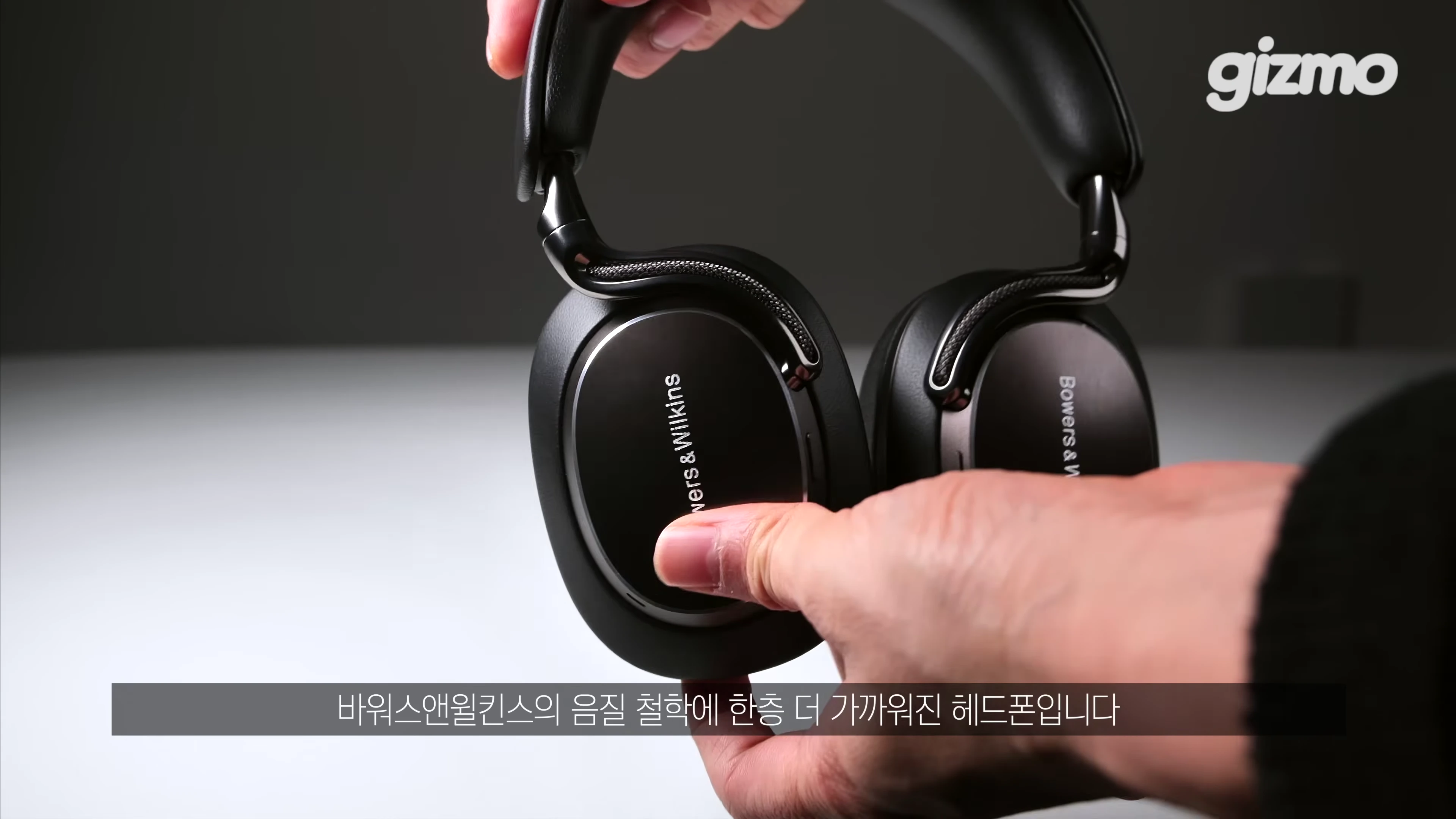 손으로 검은색 바워스앤윌킨스 헤드폰을 들고 있는 모습