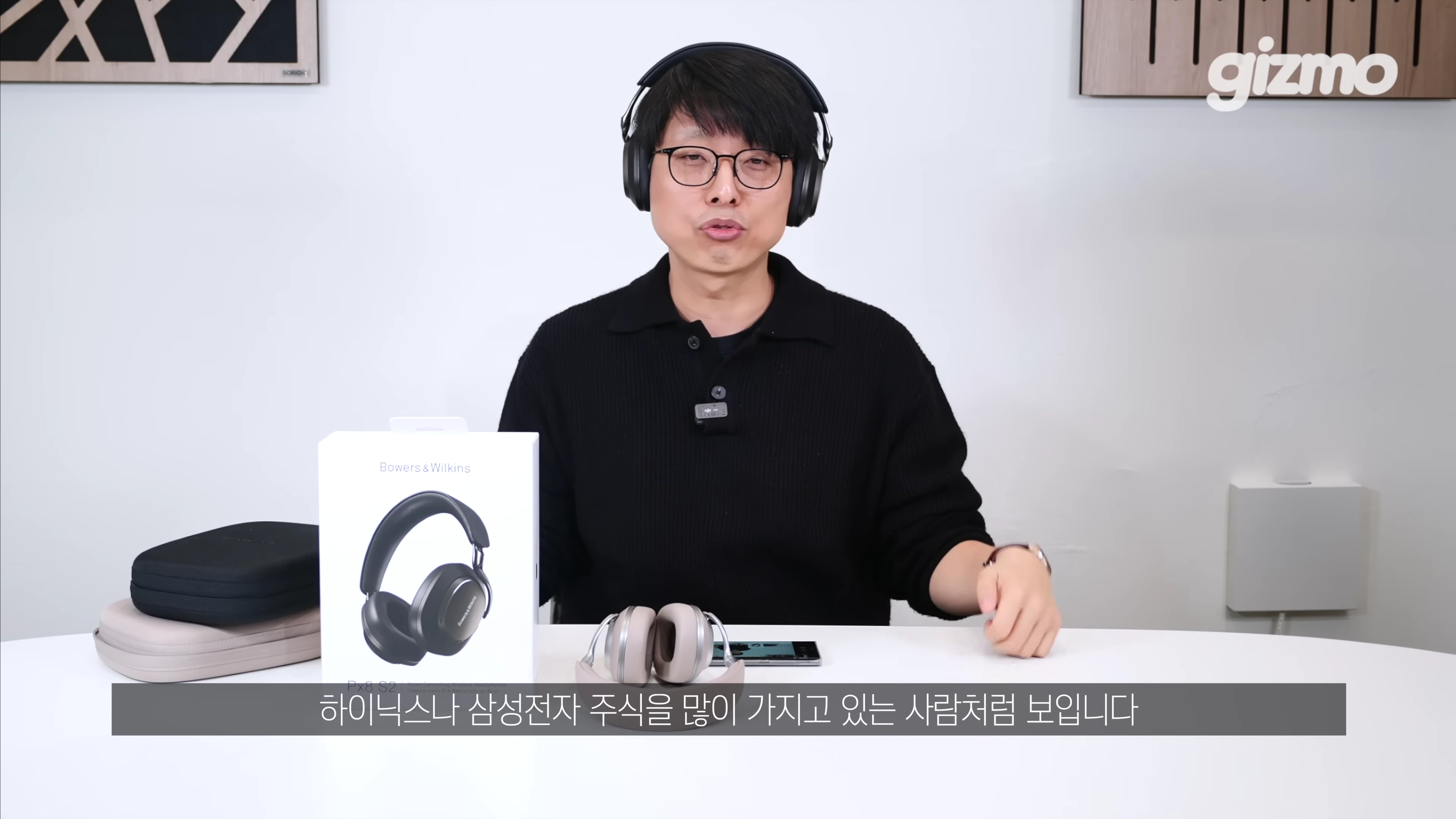 헤드폰을 착용한 안경 쓴 남성이 책상 앞에 앉아 제품을 소개하는 모습