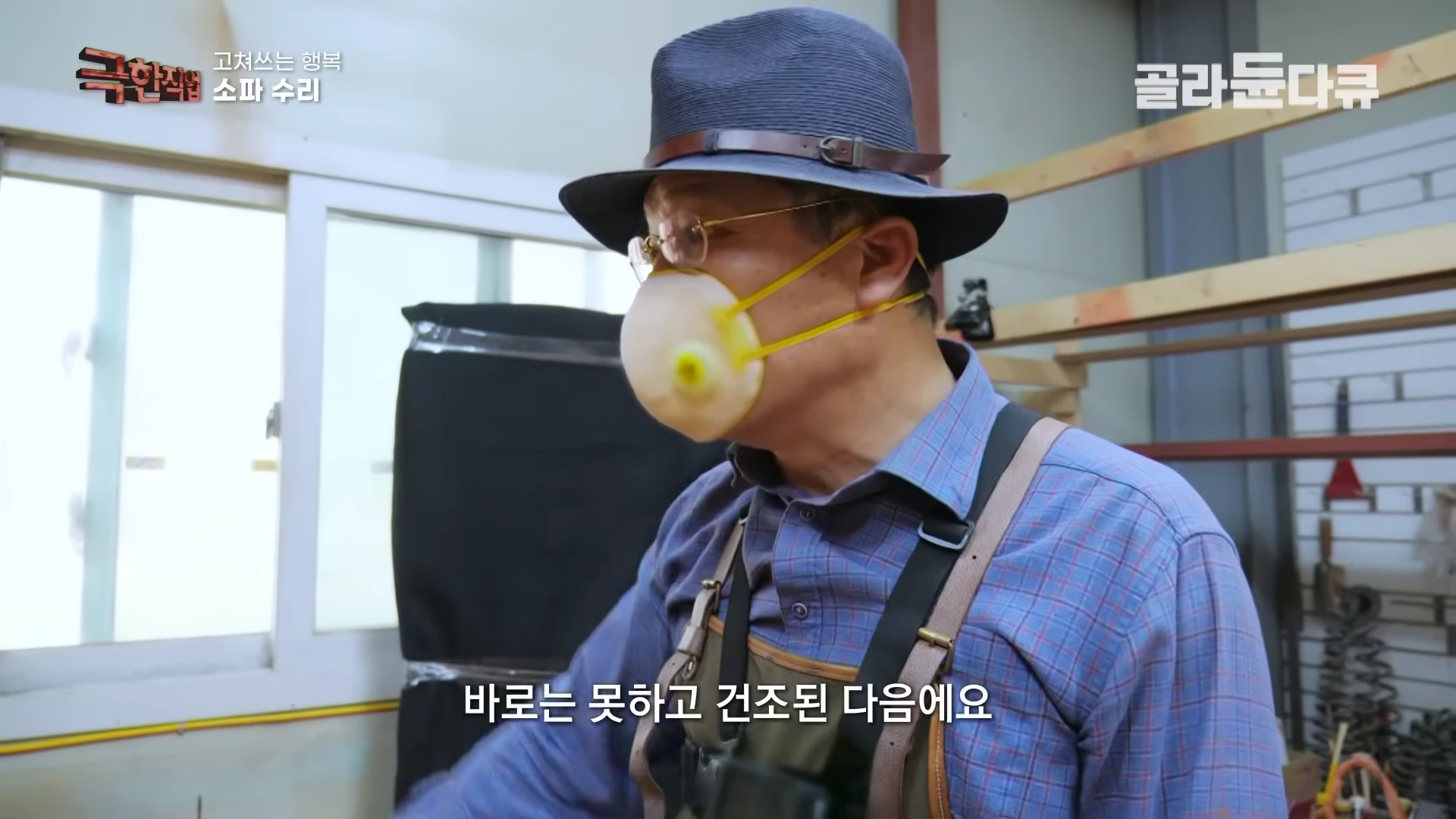 작업실에서 페도라를 쓰고 방진 마스크를 착용한 중년 남성이 소파 수리 작업을 하고 있다.