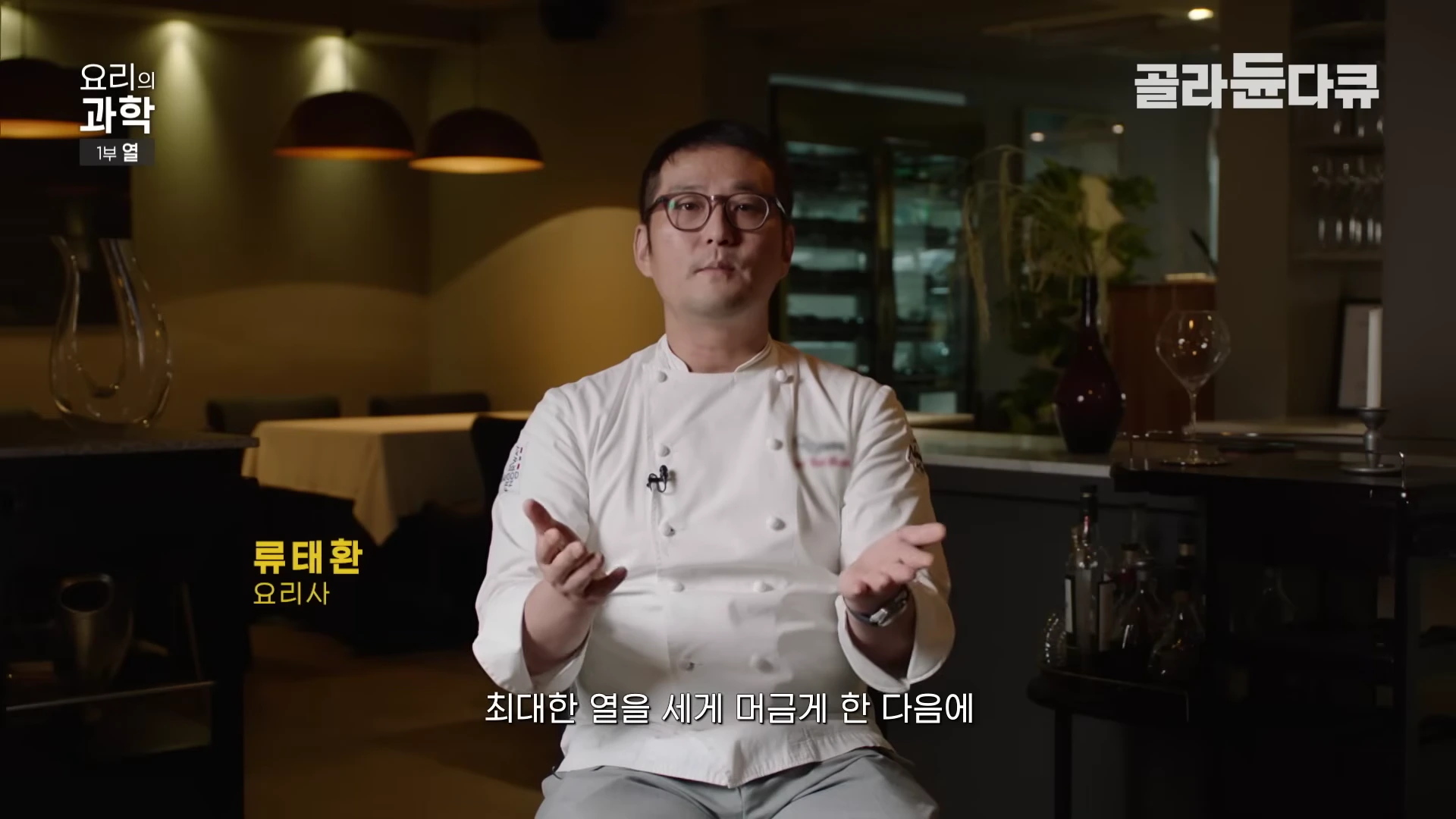 흰색 조리복을 입은 안경 쓴 요리사가 식당을 배경으로 인터뷰하는 모습