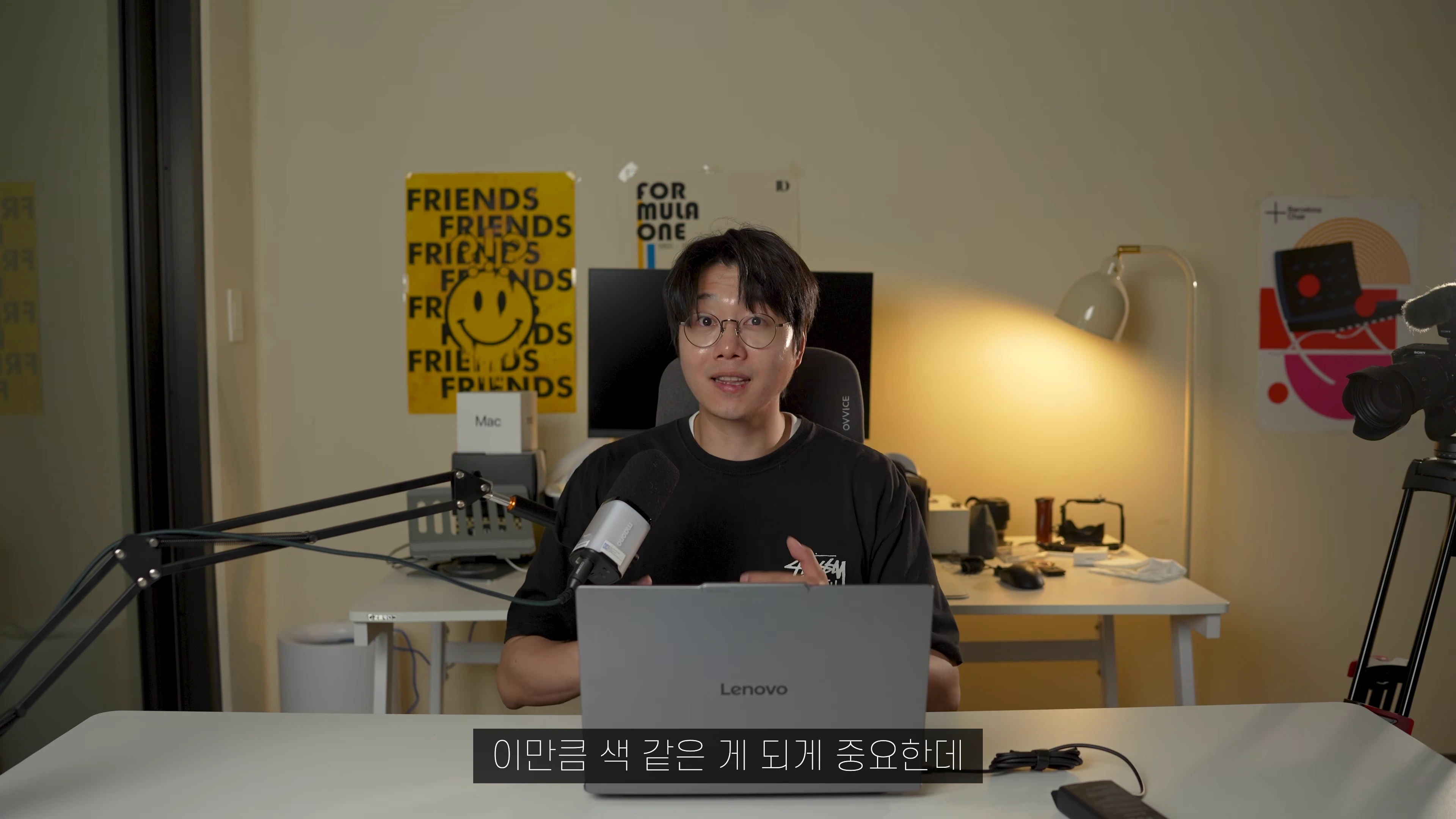 안경을 쓴 남성이 책상 앞에 앉아 노트북을 보며 이야기하는 스튜디오 촬영 장면