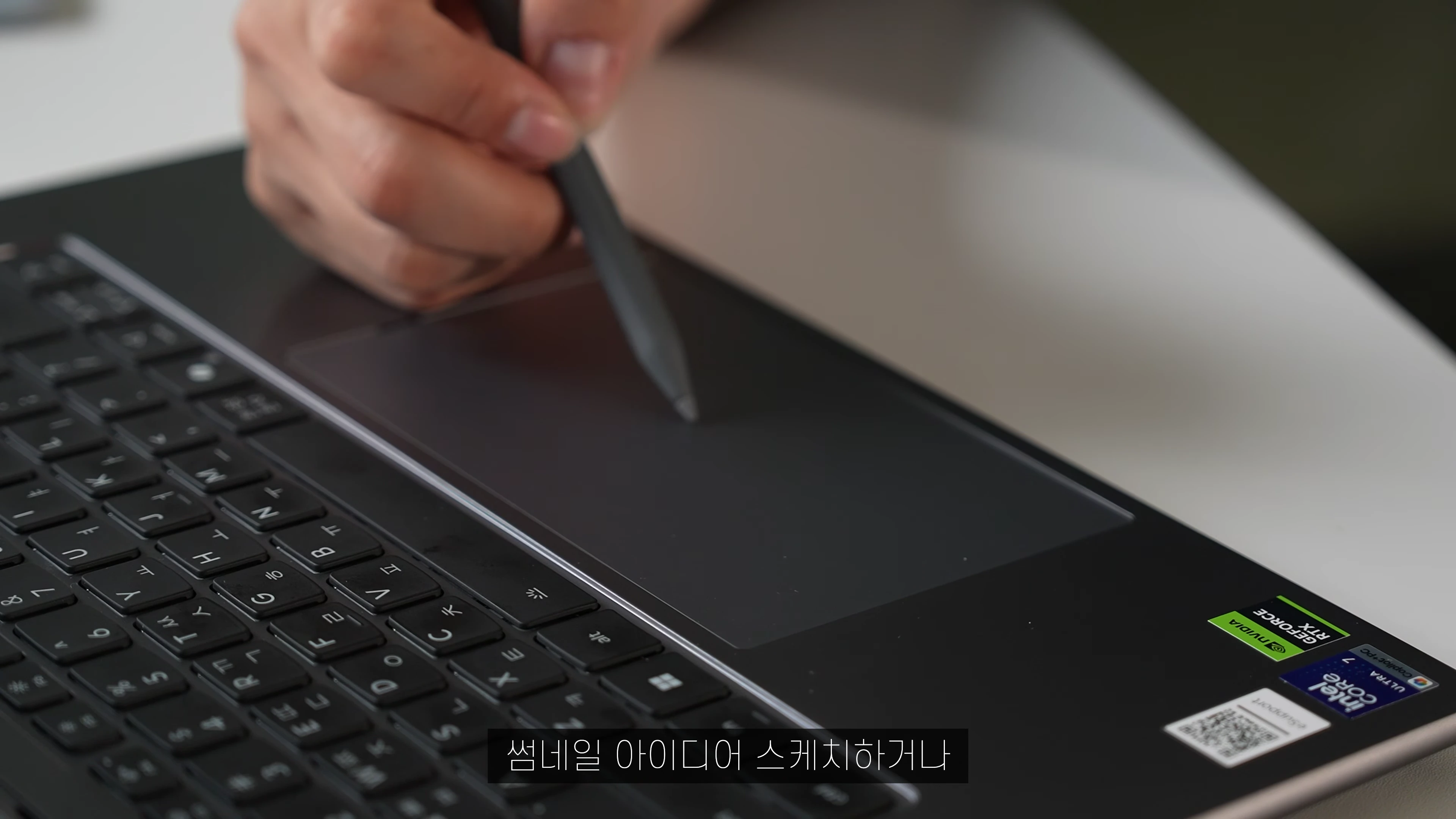 노트북 키보드 옆 트랙패드 위에서 스타일러스 펜을 사용하여 작업하는 손의 모습