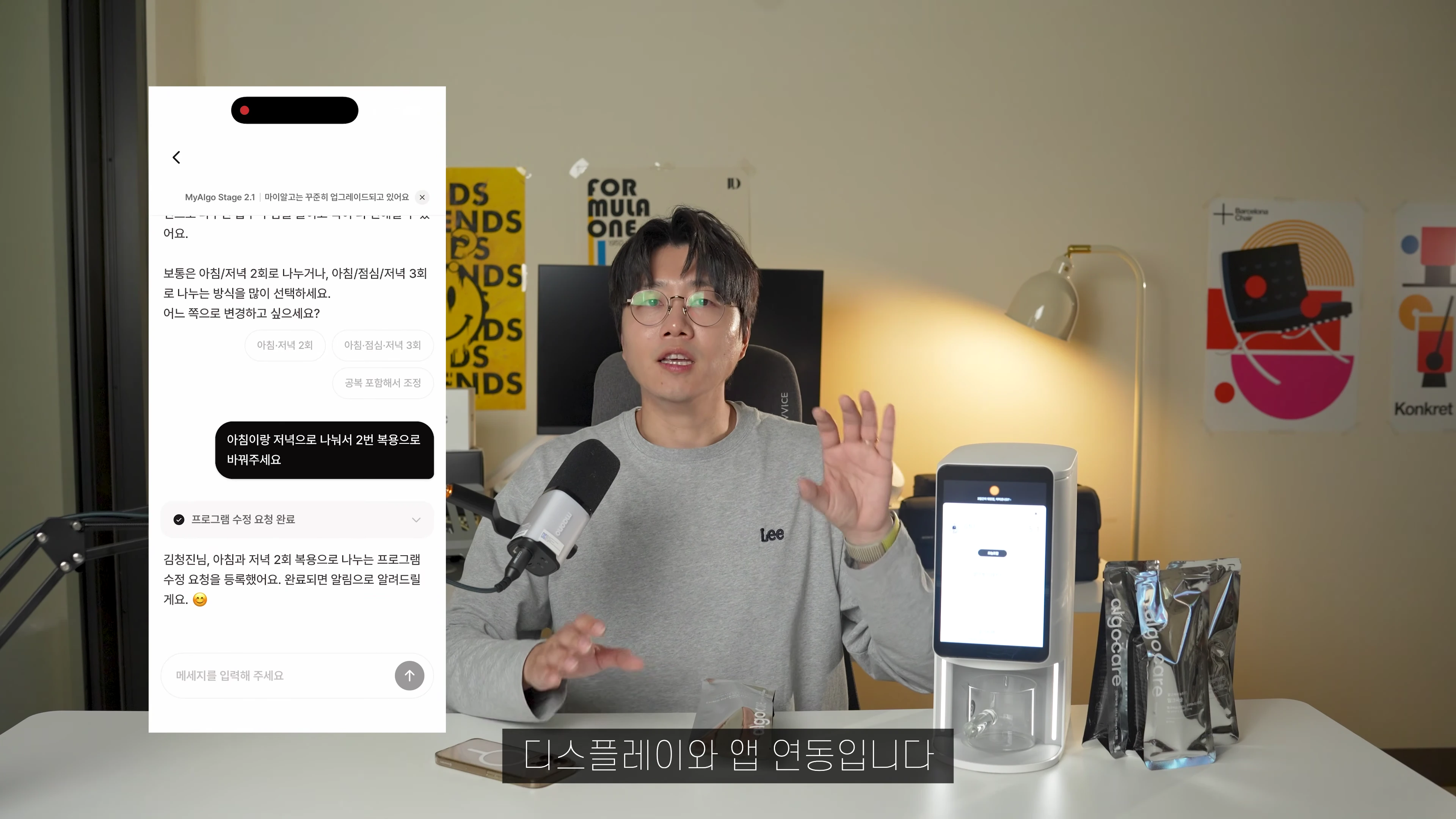 안경을 쓴 남성이 책상 앞에 앉아 있고, 옆에는 영양제 기기와 스마트폰 화면이 떠 있는 모습