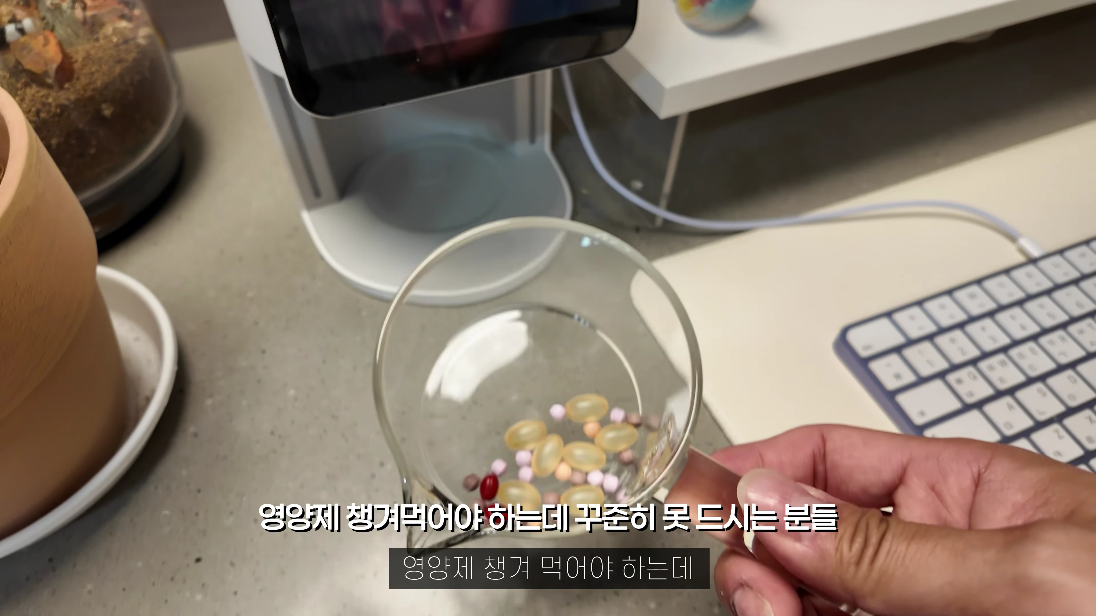 영양제가 담긴 작은 유리컵을 손으로 들고 있는 모습과 배경의 기기