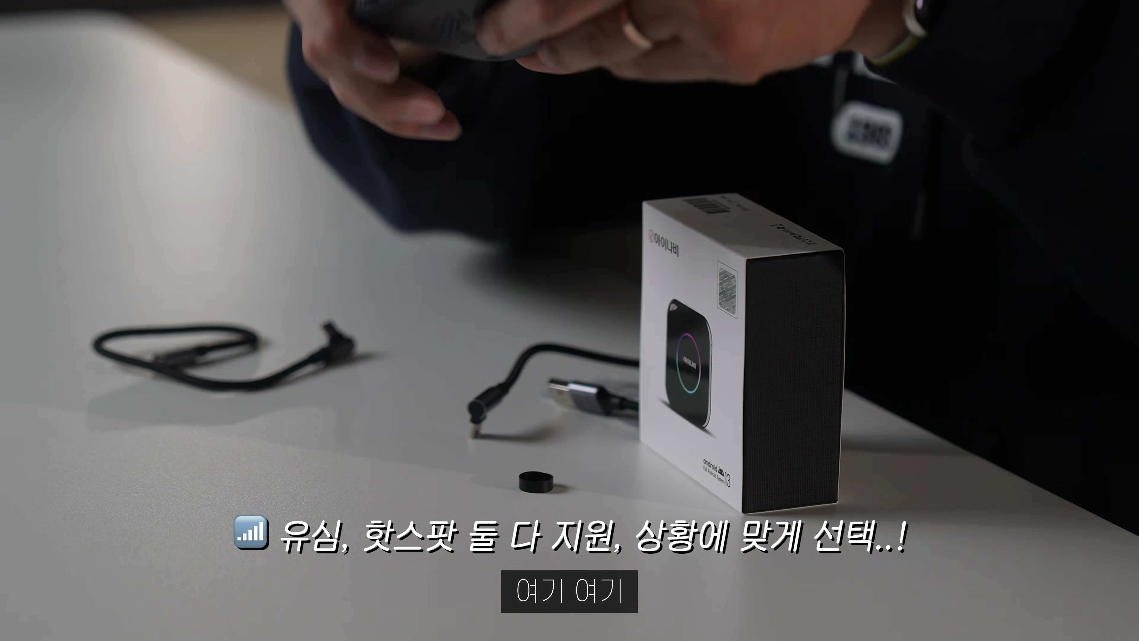 테이블 위에 놓인 제품 상자와 케이블, 그리고 손에 들린 기기를 보여주는 근접 촬영 화면