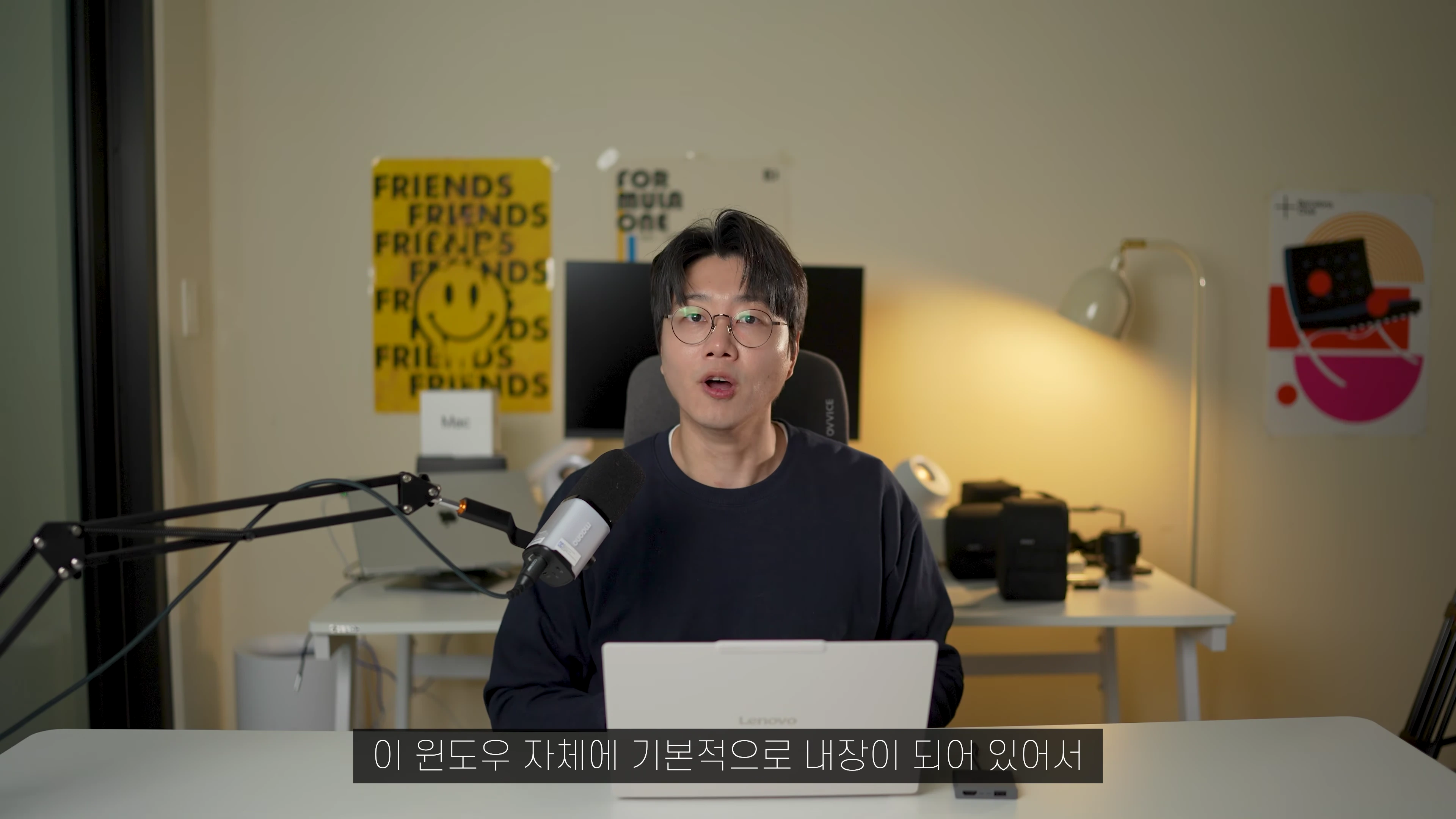 안경을 쓴 남성이 책상 앞에 앉아 노트북을 사용하며 이야기를 나누는 모습