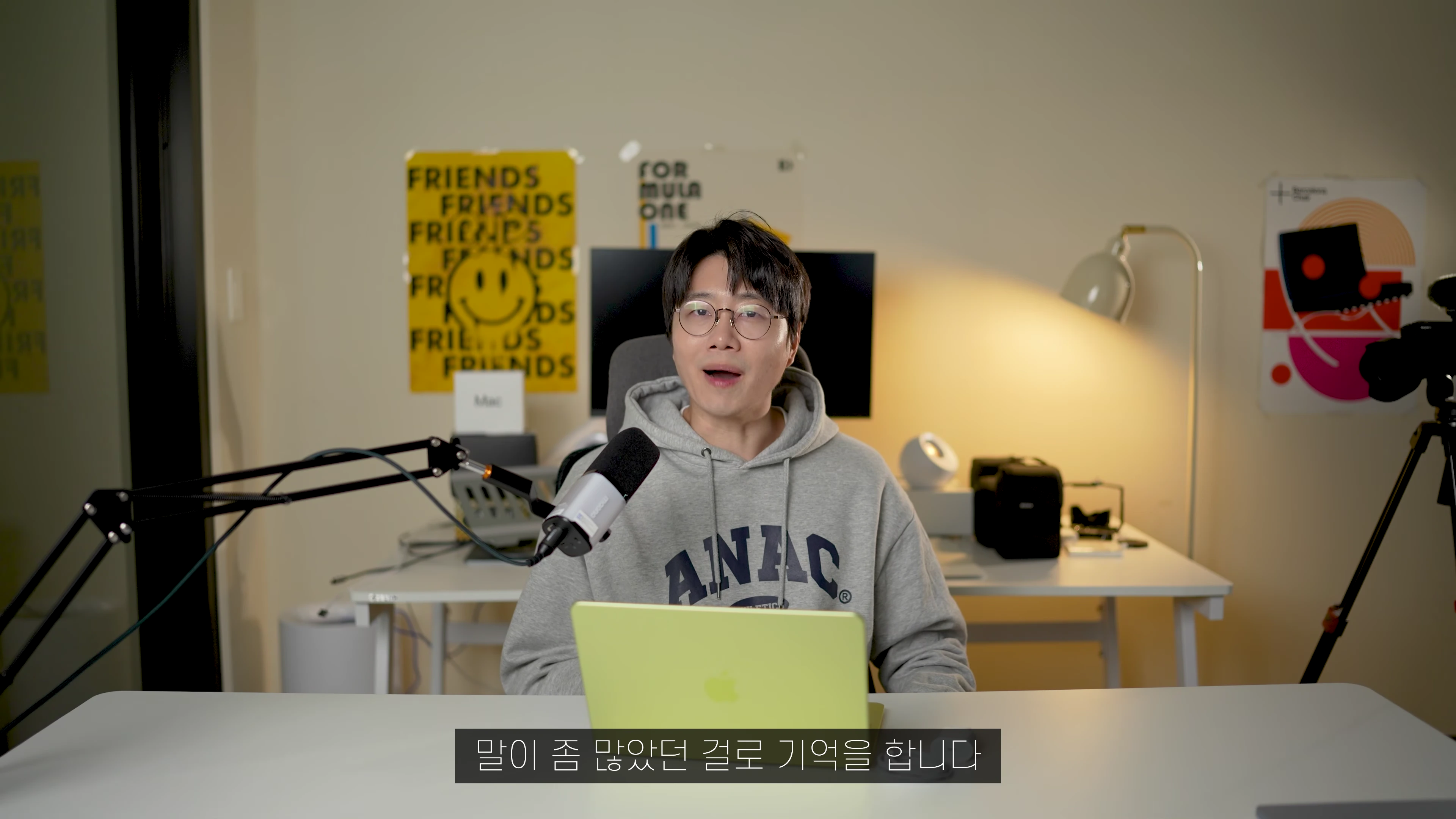 안경을 쓴 남성이 라임색 노트북 앞에 앉아 마이크를 향해 이야기하는 모습
