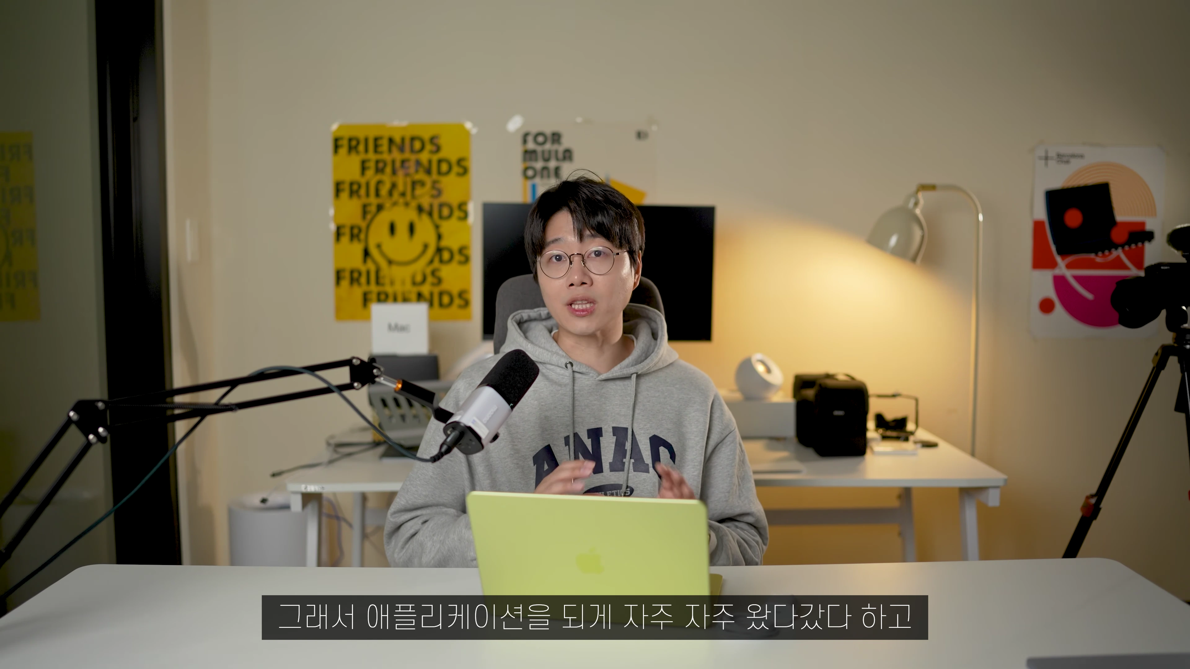 안경을 쓴 남성이 책상 앞에 앉아 마이크를 앞에 두고 이야기를 나누는 모습