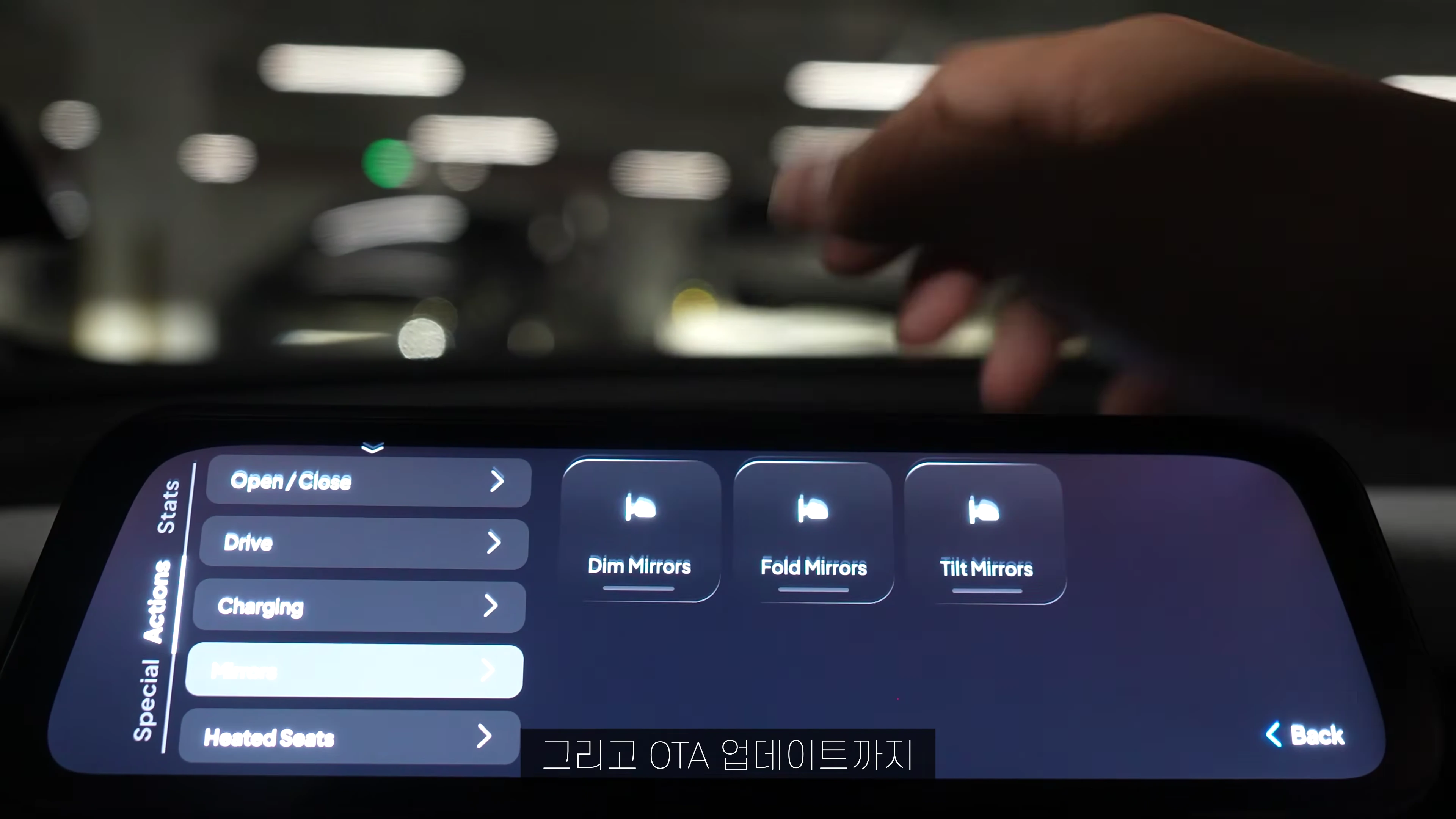차량 대시보드에 설치된 디스플레이 화면에 사이드미러 제어 메뉴가 나타나 있고, 손이 화면 근처에 위치해 있다.