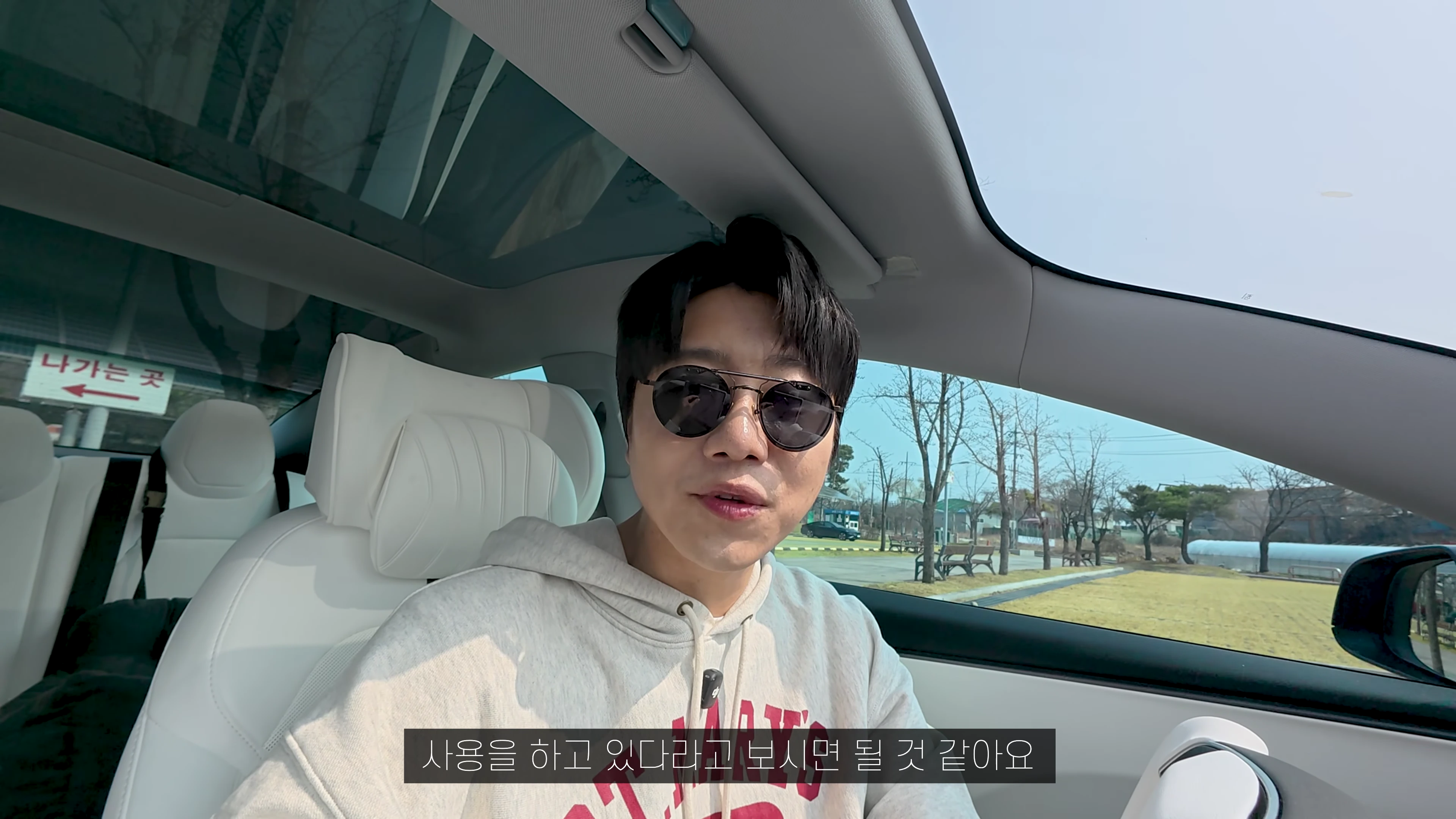 선글라스를 쓴 남성이 테슬라 차량 운전석에 앉아 카메라를 응시하고 있다.