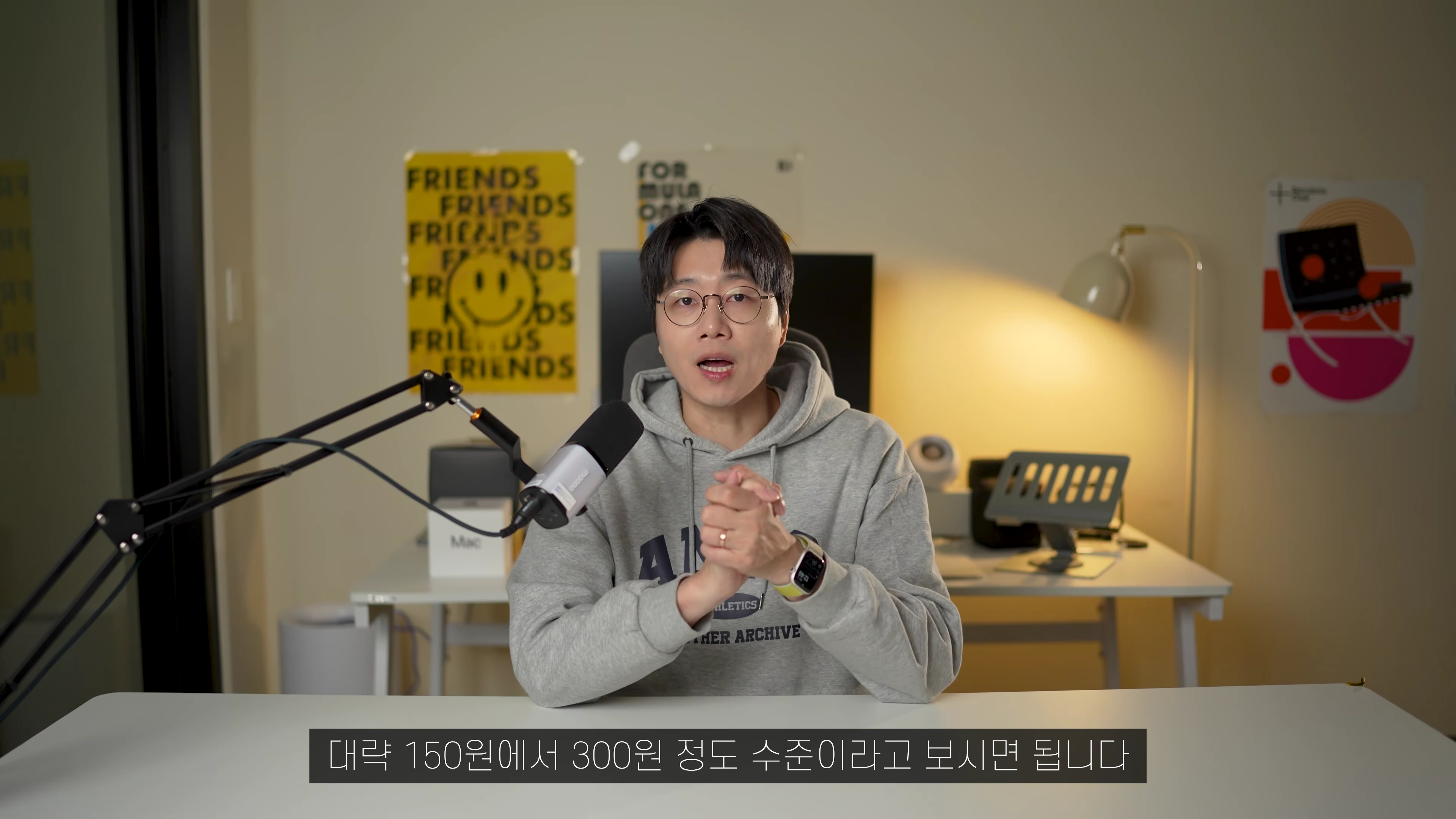안경을 쓴 남성이 책상 앞에 앉아 마이크를 앞에 두고 이야기하는 모습