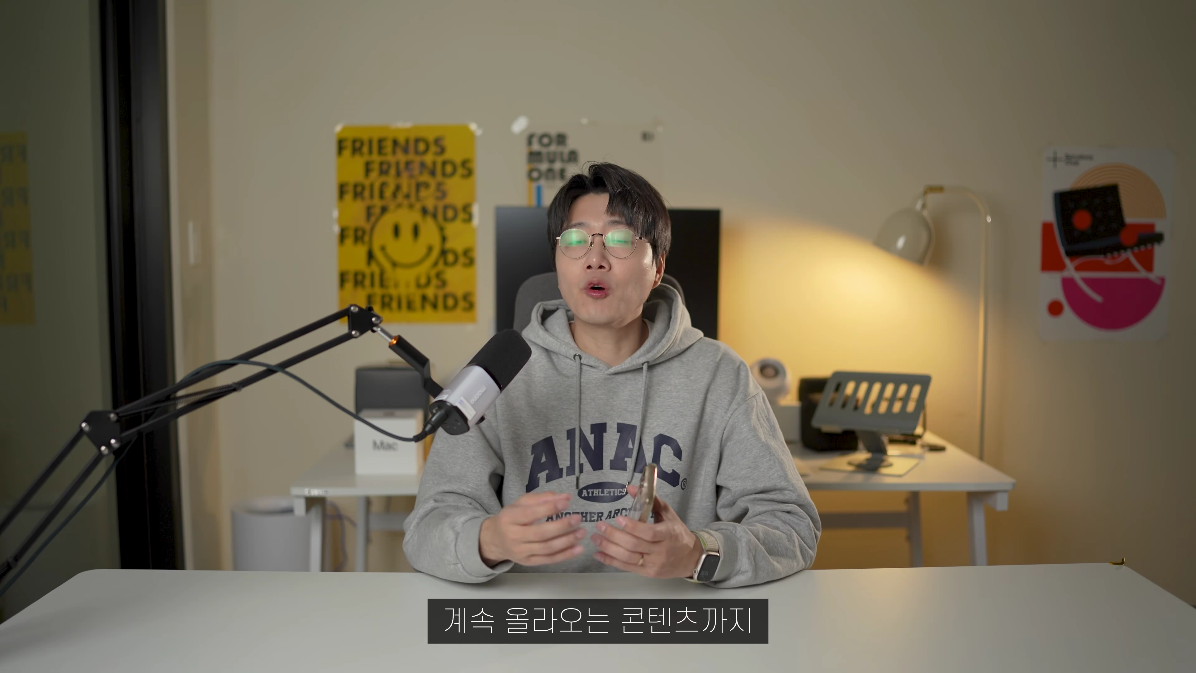 안경을 쓴 남성이 책상 앞에 앉아 마이크를 앞에 두고 이야기하는 모습
