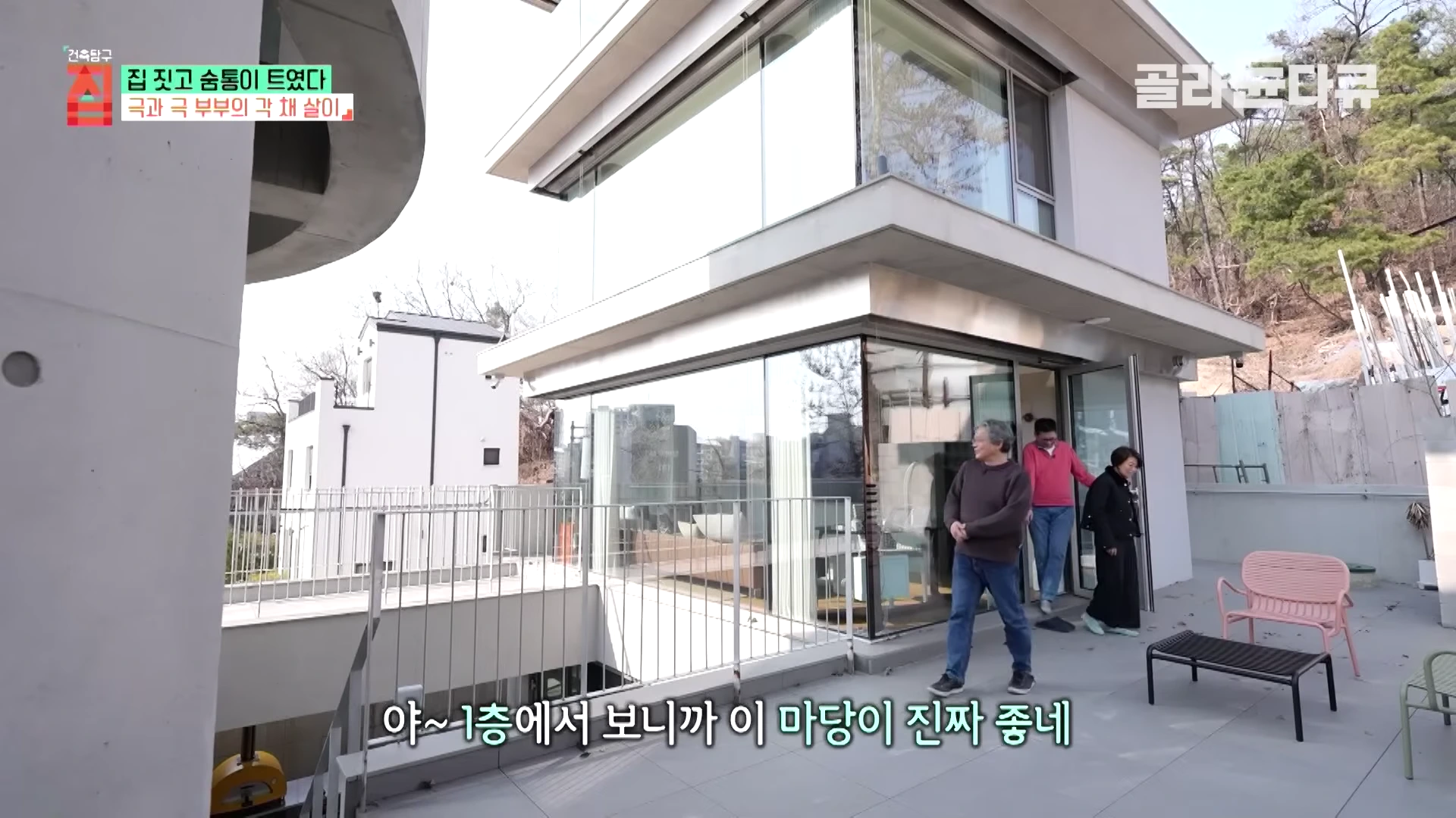 통유리로 된 현대적인 주택 테라스에서 세 사람이 대화를 나누며 걷고 있는 모습