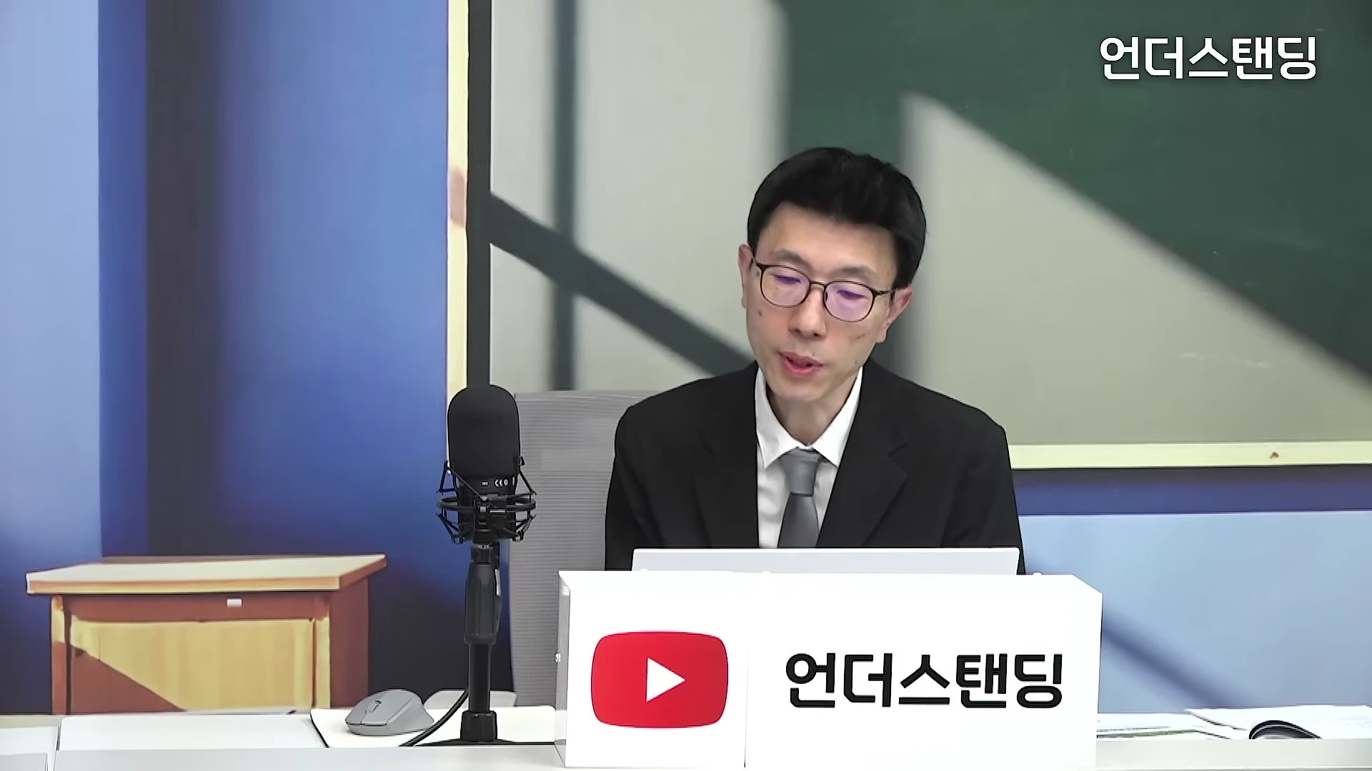 안경을 쓴 남성이 스튜디오에서 마이크 앞에 앉아 이야기를 나누고 있는 모습