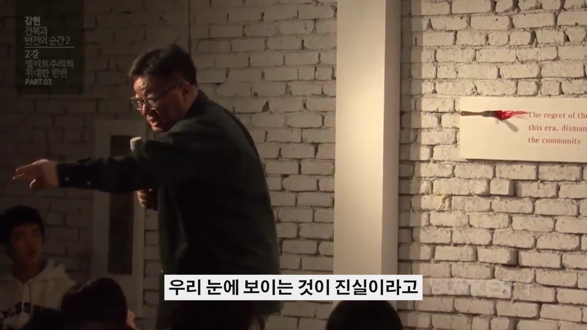 강연장에서 마이크를 든 남성이 청중을 향해 손짓하며 열정적으로 이야기하고 있다.