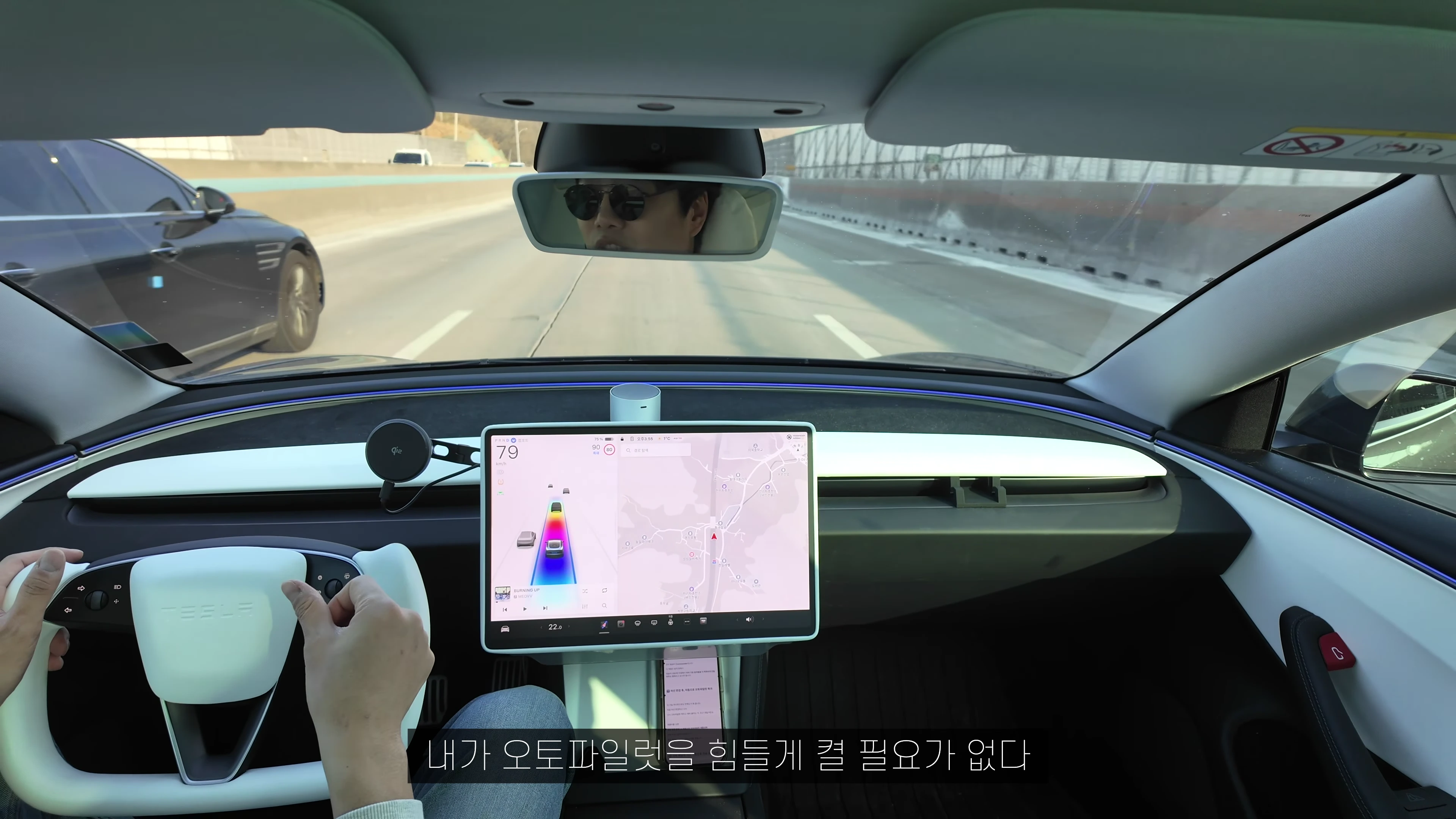 테슬라 차량 내부에서 운전자가 요크 핸들을 잡고 주행 중인 모습
