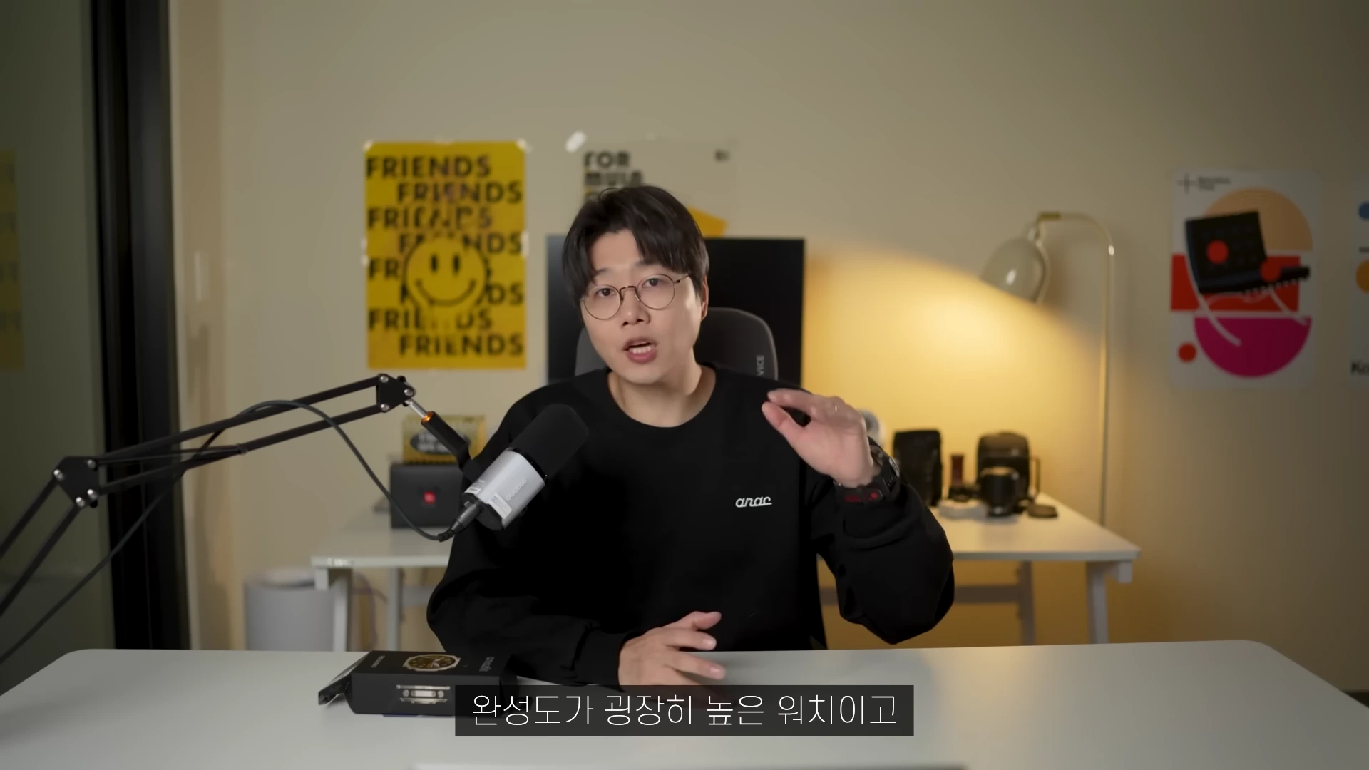 안경을 쓴 남성이 마이크 앞에 앉아 손짓하며 이야기하는 모습