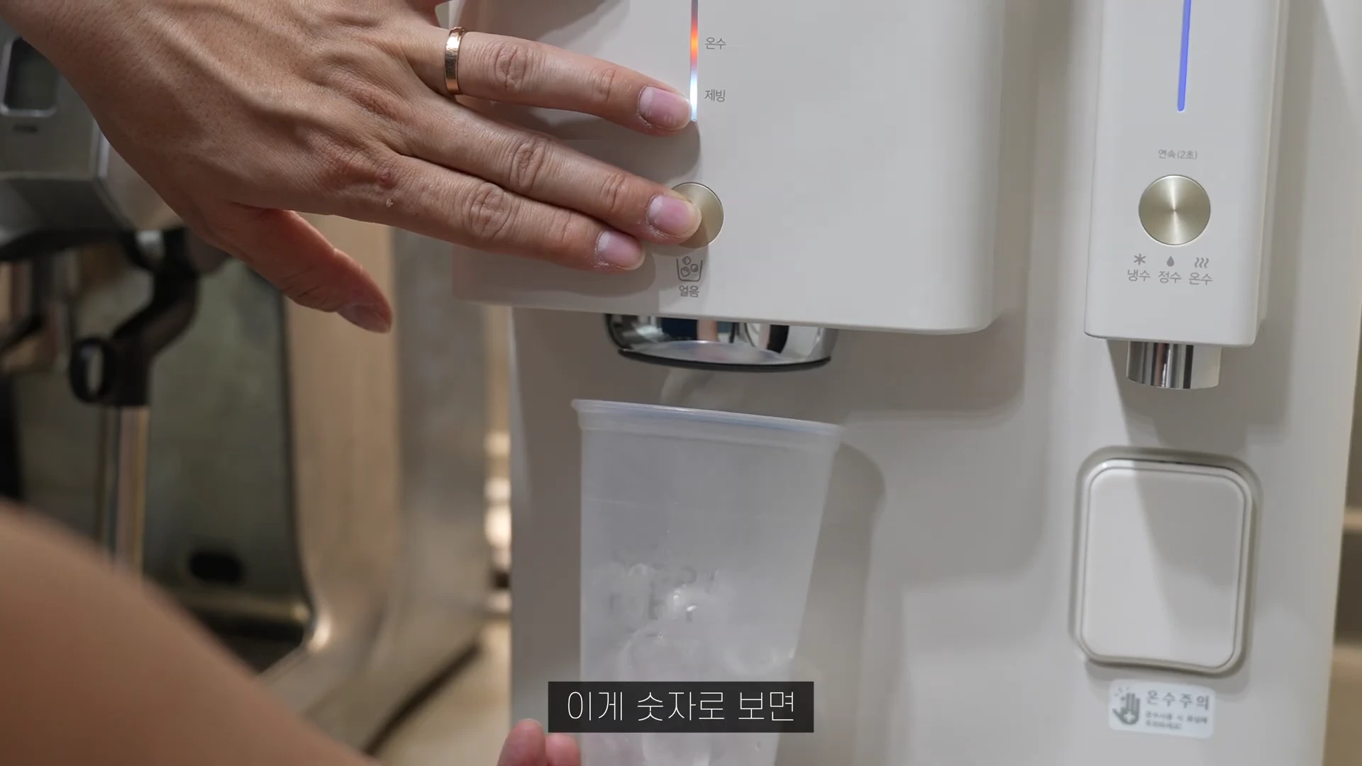 흰색 얼음 정수기 버튼을 눌러 투명한 컵에 얼음을 받는 모습