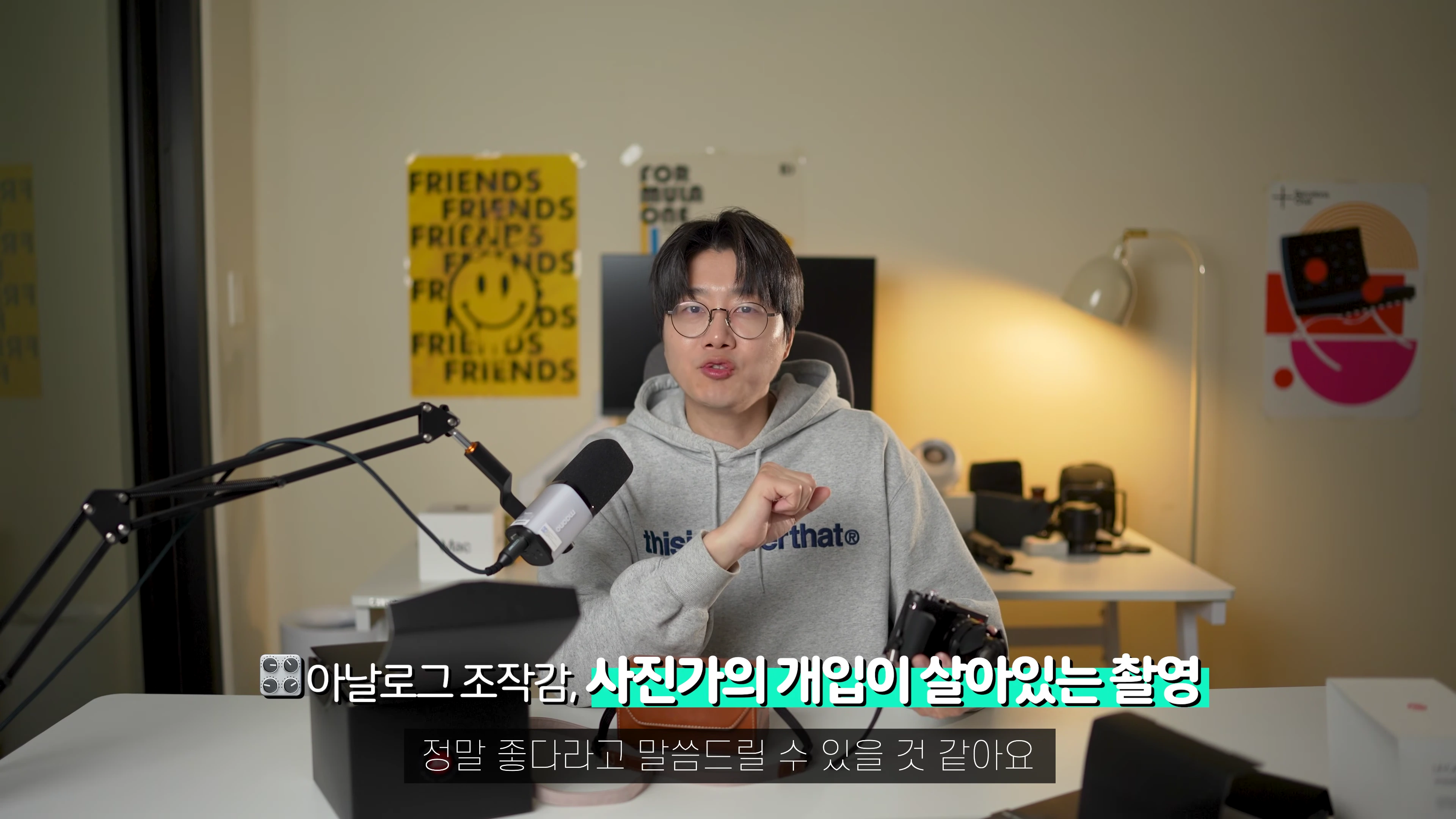 안경을 쓴 남성이 책상에 앉아 카메라를 들고 설명하는 모습