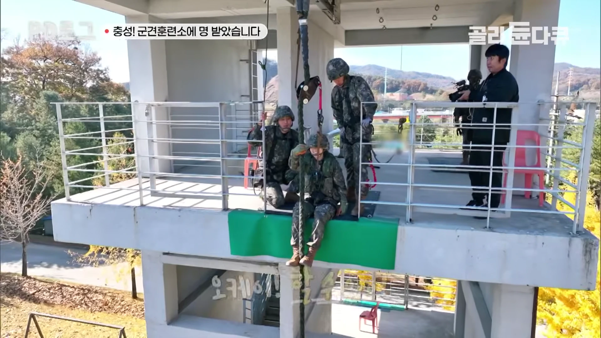 군복을 입은 사람들이 높은 훈련탑에서 로프를 이용해 하강 훈련을 준비하고 있다.