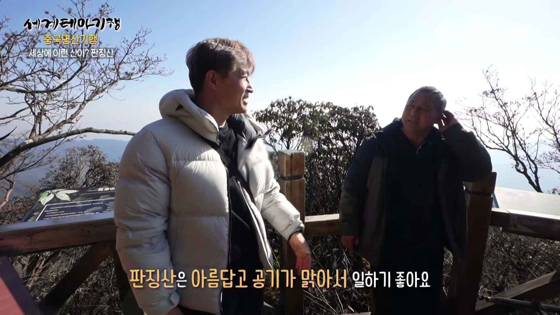 야외 산 정상에서 두 남성이 서서 대화를 나누고 있는 모습