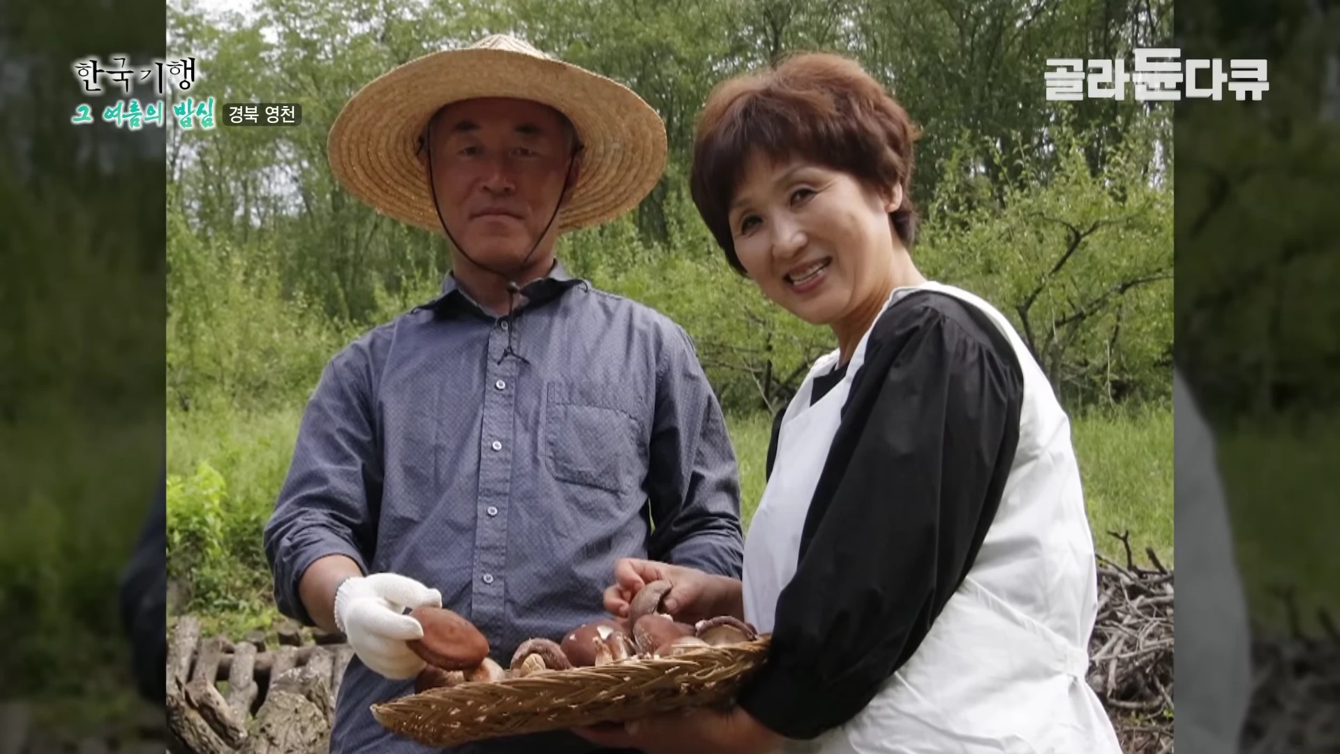 밀짚모자를 쓴 남성과 앞치마를 두른 여성이 숲속에서 버섯이 담긴 바구니를 함께 들고 있다.