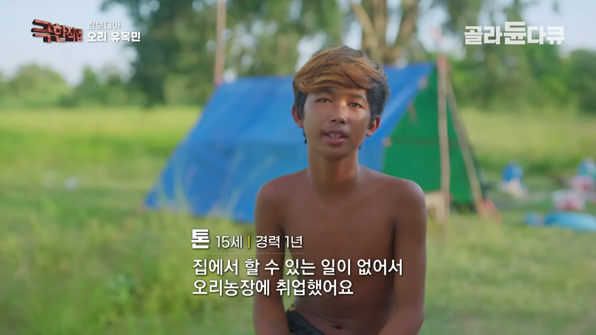 야외 들판에 설치된 파란색 텐트를 배경으로 한 소년이 인터뷰하고 있는 모습
