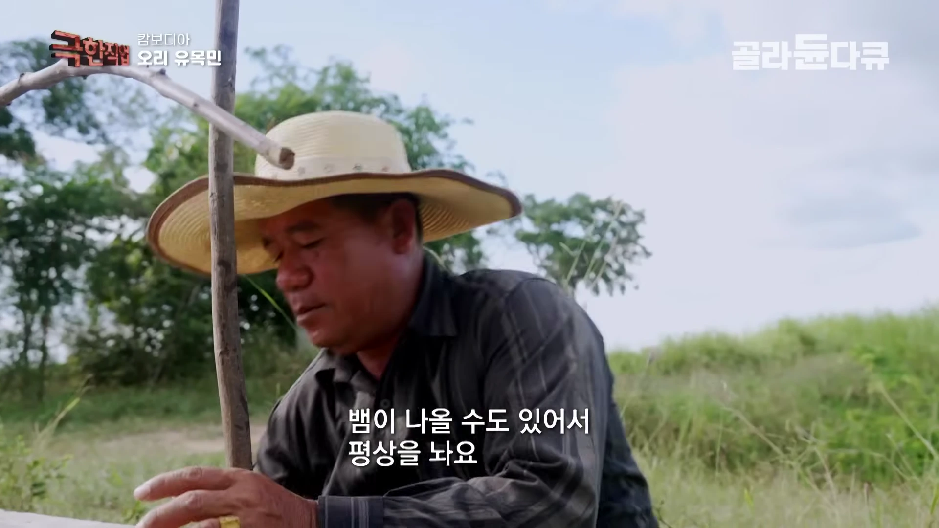 밀짚모자를 쓴 남성이 야외 논밭에서 나무 막대기를 잡고 작업하는 모습
