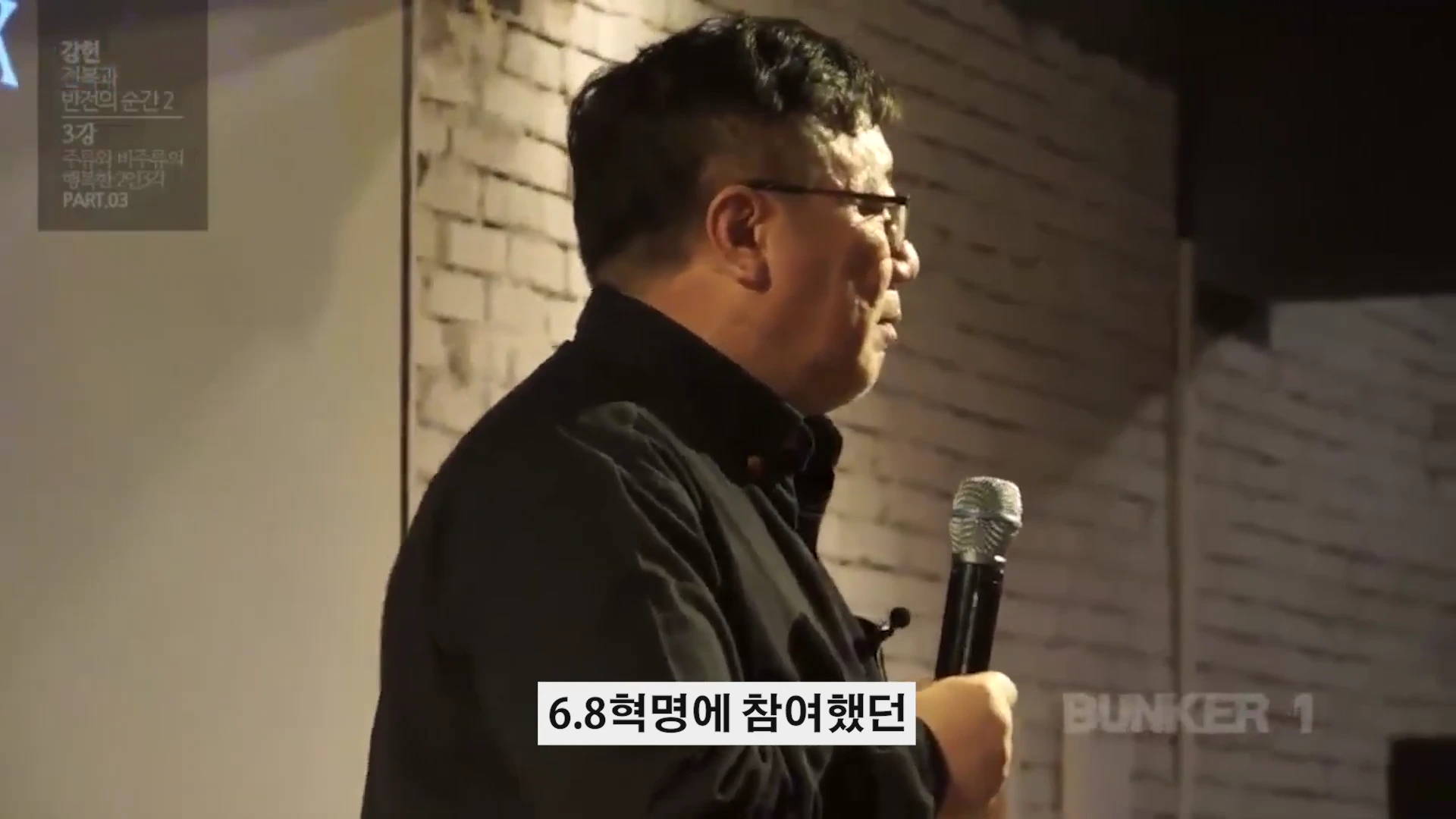 안경을 쓴 중년 남성이 마이크를 들고 강연하는 옆모습