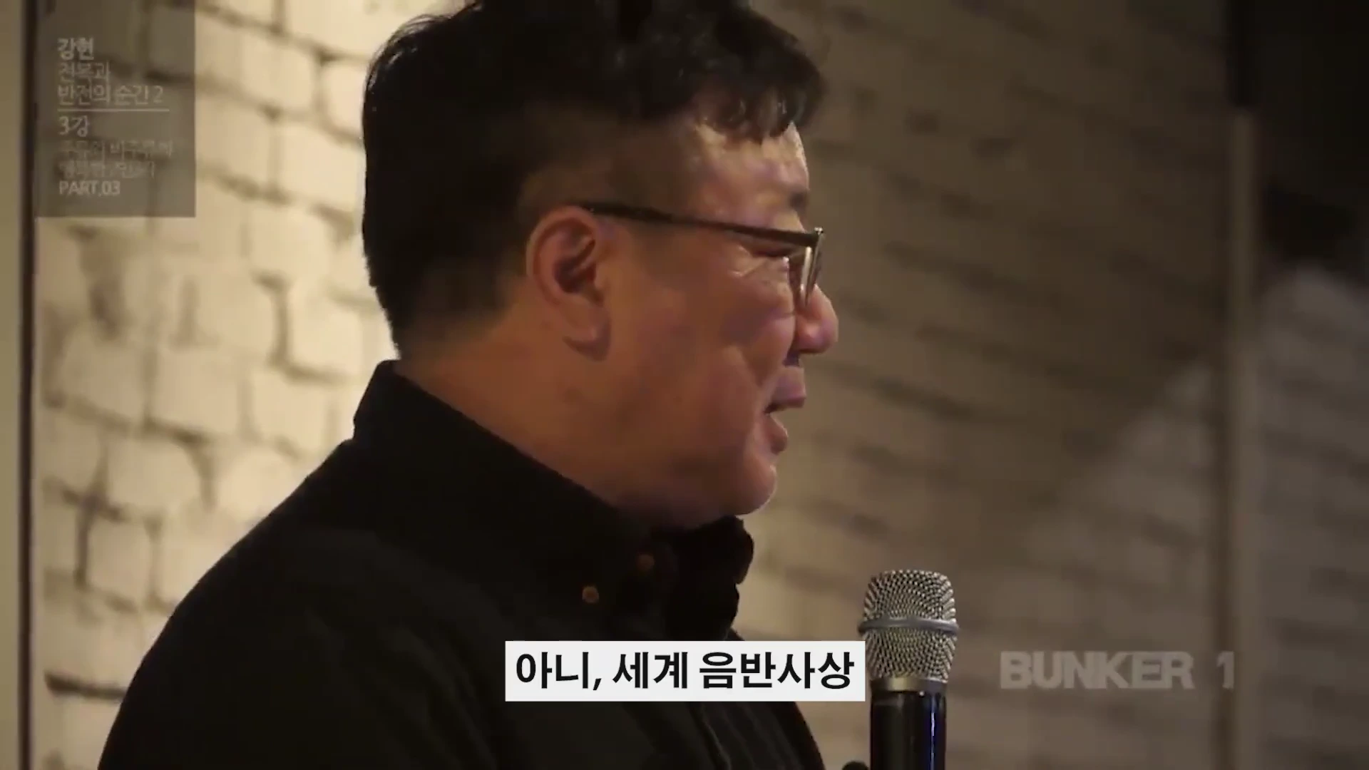 안경을 쓴 중년 남성이 마이크를 잡고 강연하는 옆모습