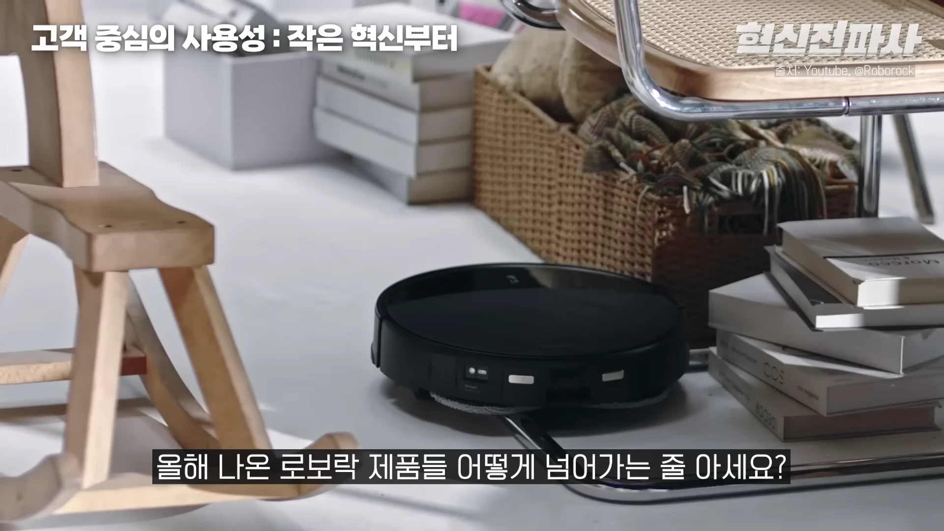실내 바닥에서 검은색 원형 로봇청소기가 가구 사이를 지나가는 모습이 담긴 영상 캡처 화면