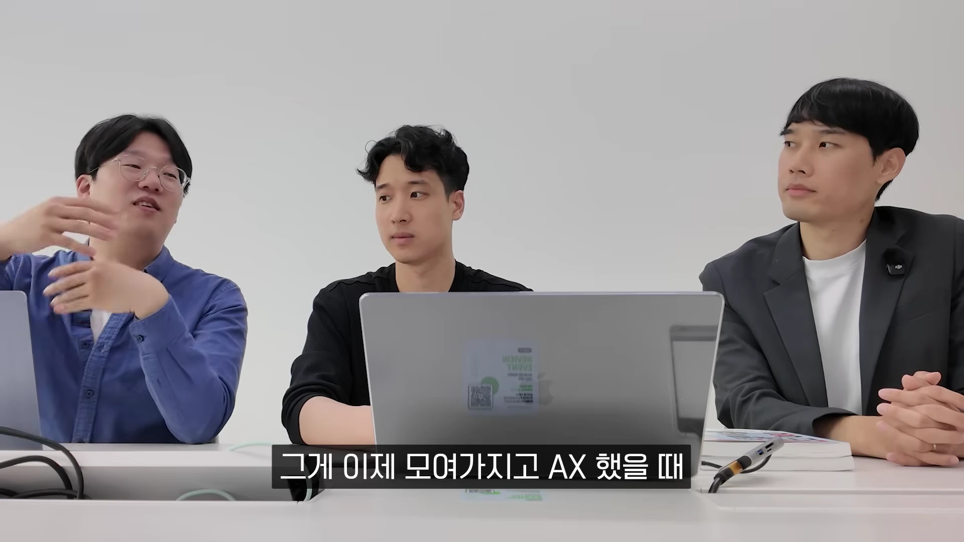 세 명의 남성이 테이블에 앉아 노트북을 보며 대화하는 모습