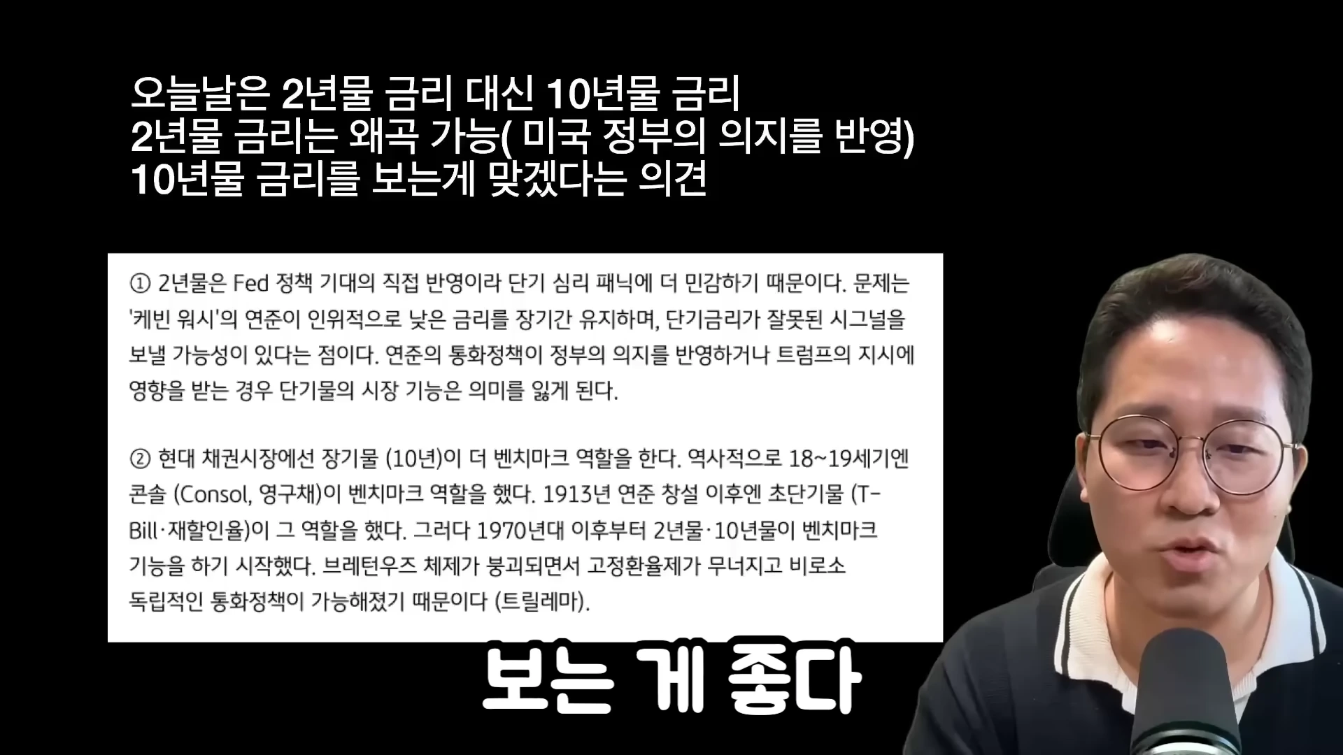 안경을 쓴 남성이 마이크 앞에서 2년물과 10년물 국채 금리 비교에 관한 텍스트가 적힌 화면을 배경으로 설명하고 있다.