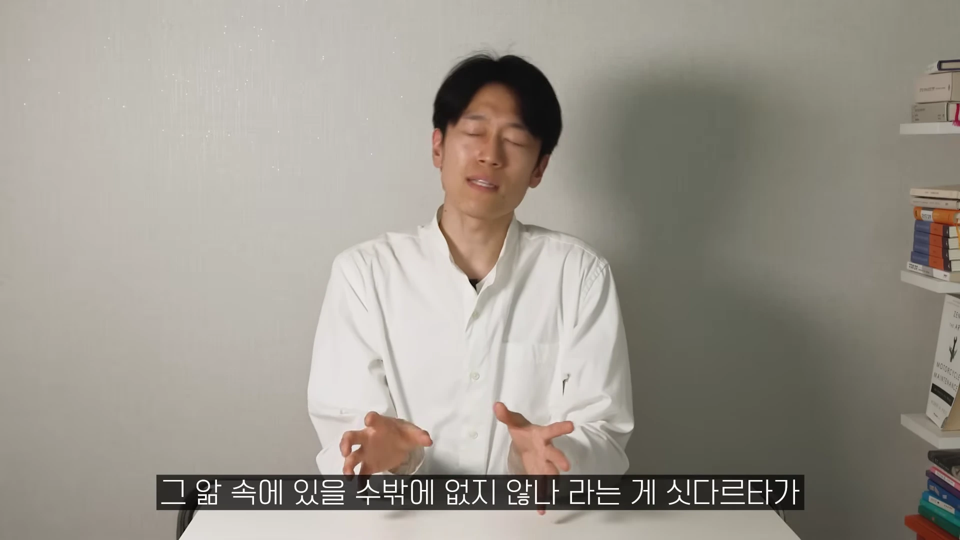 흰 셔츠를 입은 남성이 눈을 감고 손을 움직이며 이야기하는 모습
