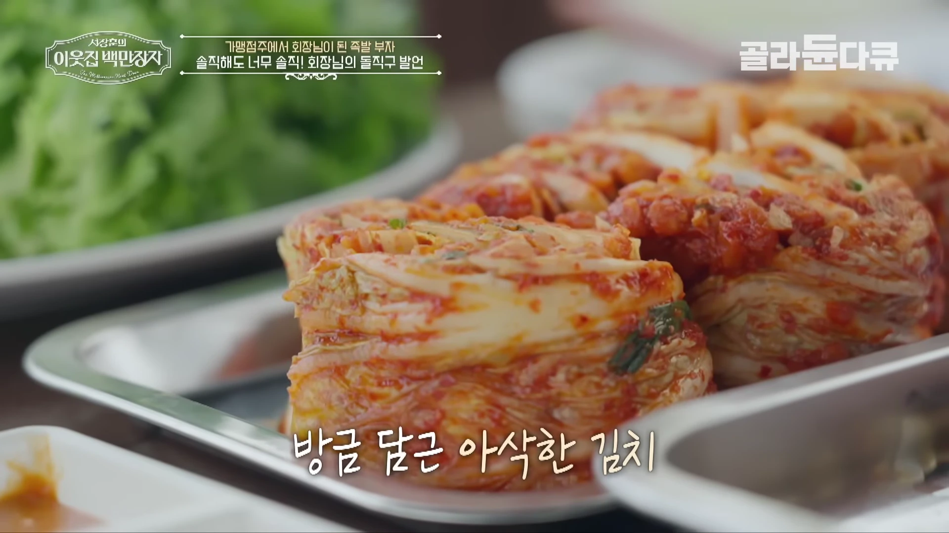 금속 쟁반 위에 먹음직스럽게 담긴 빨간 배추김치와 배경의 상추가 보이는 영상 화면