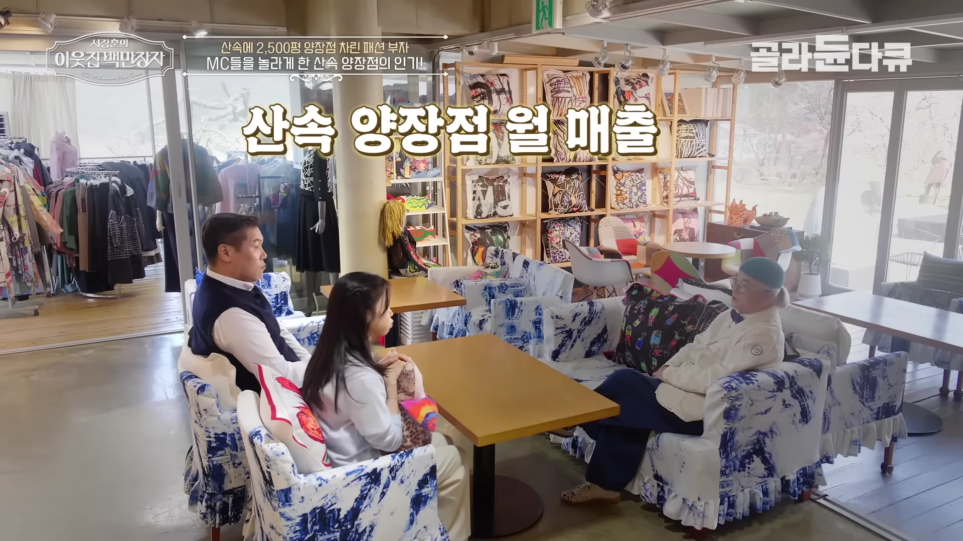 산속 양장점 내부에서 세 사람이 테이블에 둘러앉아 대화를 나누고 있으며, 주변에는 옷과 소품들이 진열되어 있다.