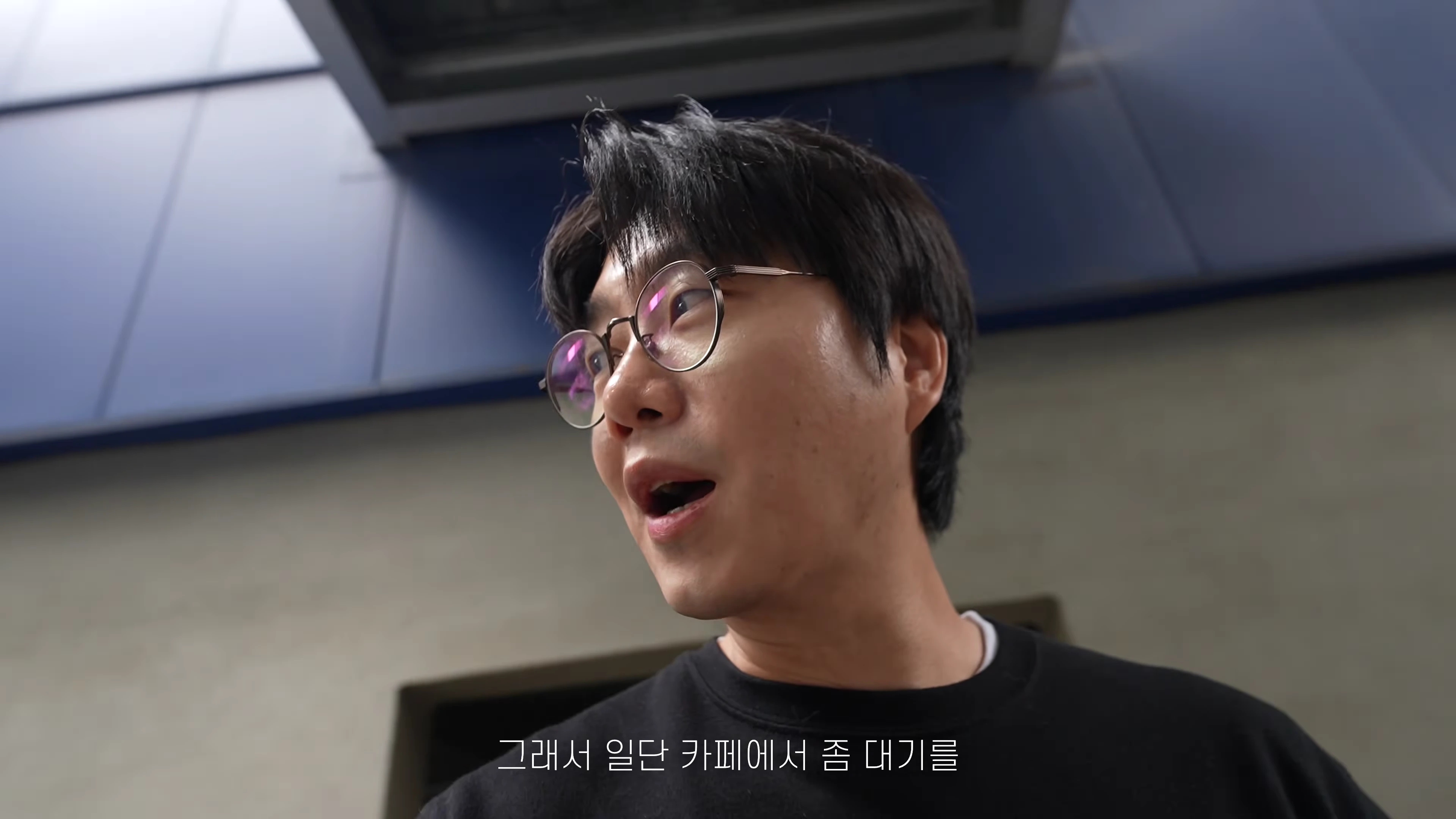 안경을 쓴 남성이 야외에서 놀란 표정으로 어딘가를 바라보고 있는 모습