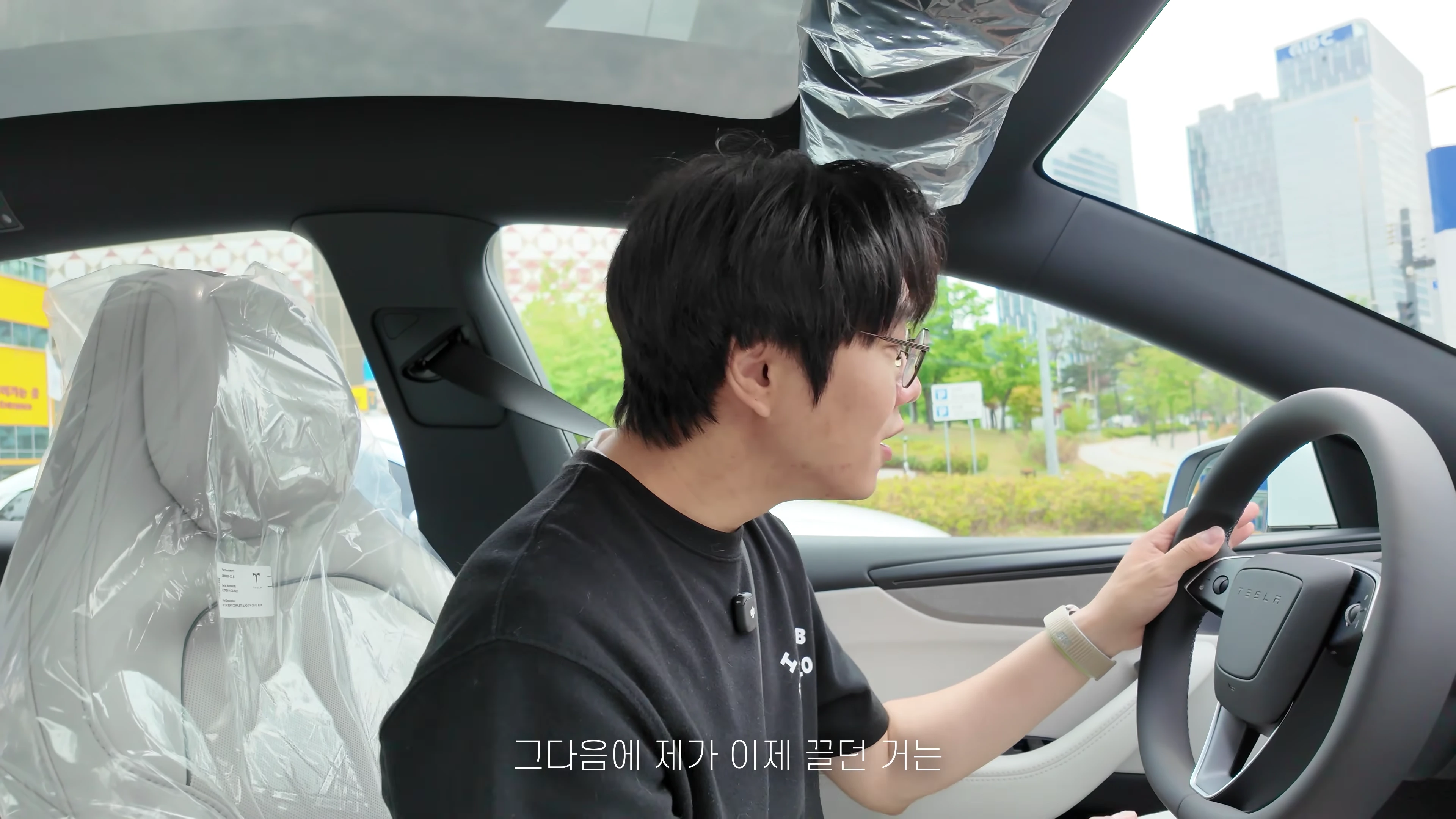 안경을 쓴 남성이 비닐이 씌워진 테슬라 차량 운전석에 앉아 핸들을 잡고 주행하는 모습